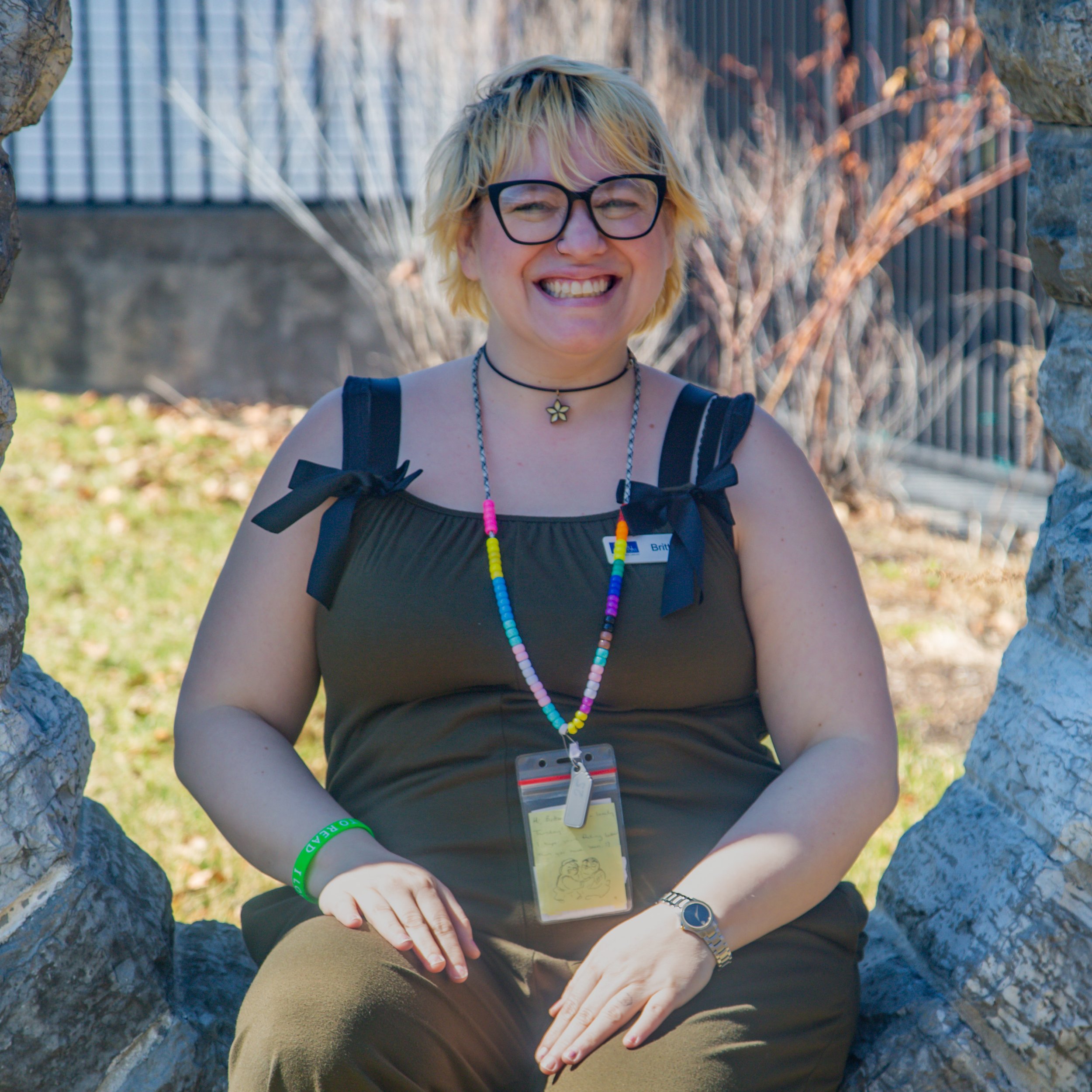 Woman with blonde hair and glasses sits in a stone circle. She wears a dark colored top and pants