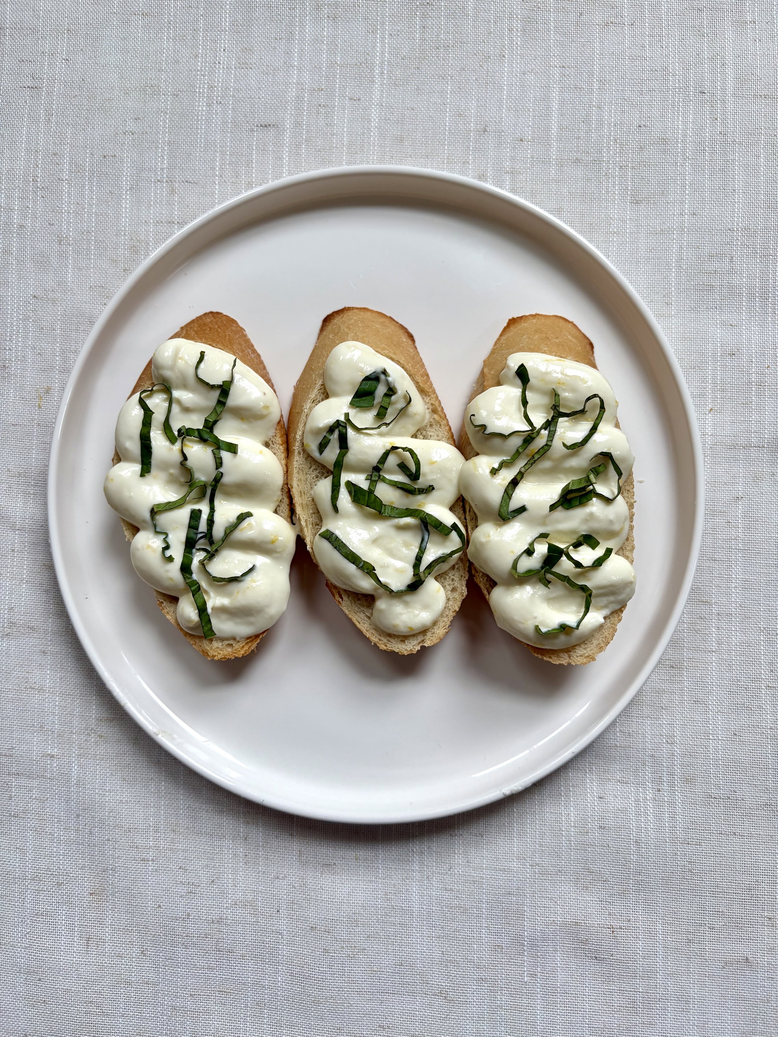 Three open-faced sandwiches on a white plate, each with a spread, topped with chopped herbs, on a white tablecloth.