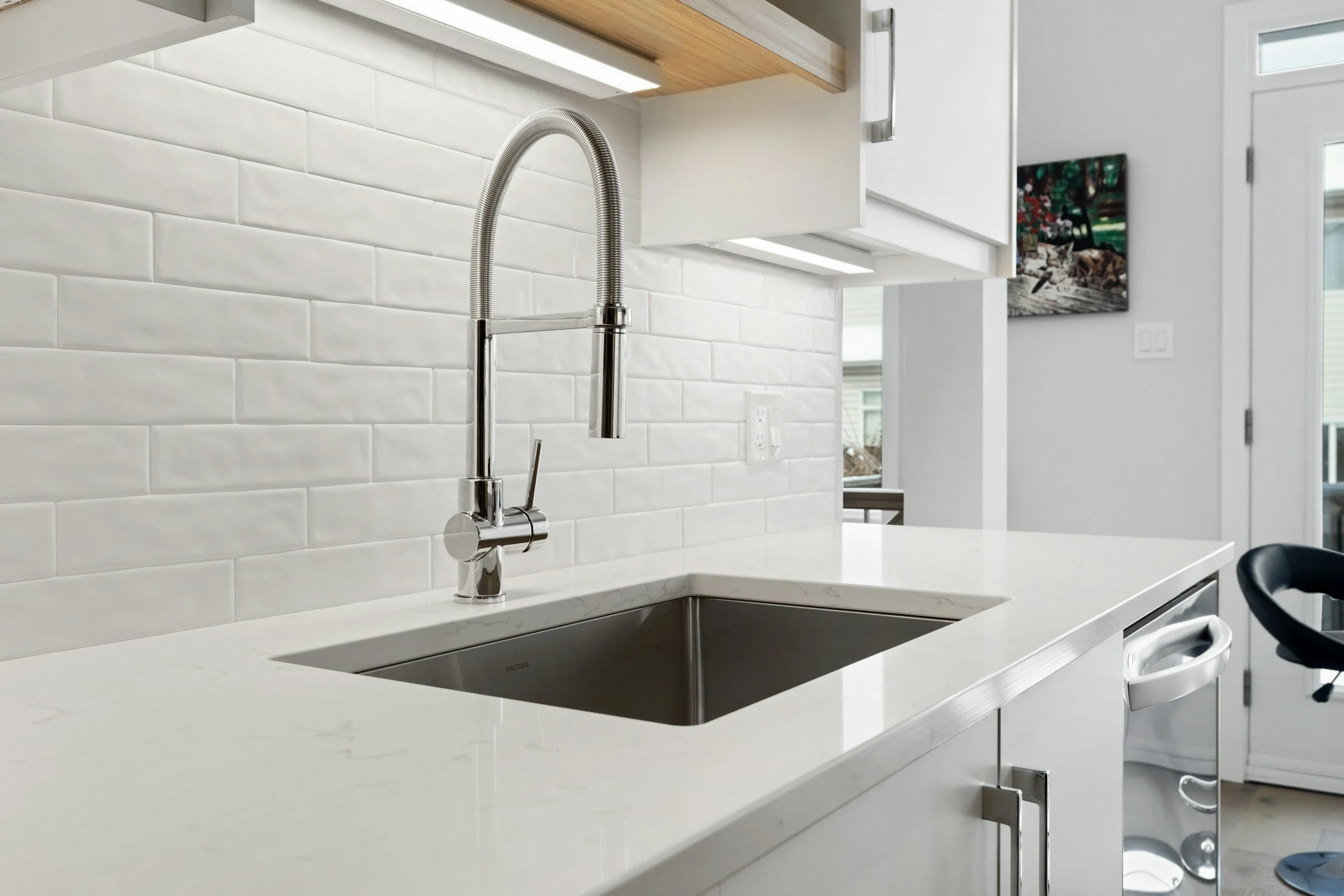 A clean white kitchen with a closeup of a sink and nice faucet