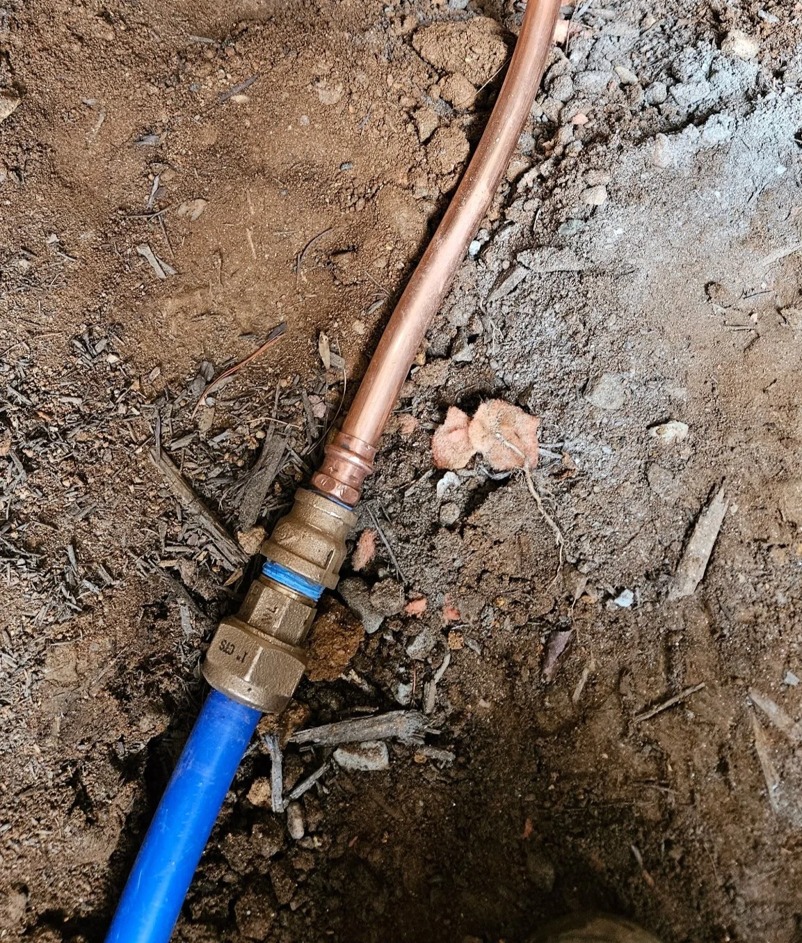 a copper pipe and a blue PEX pipe connected on the ground