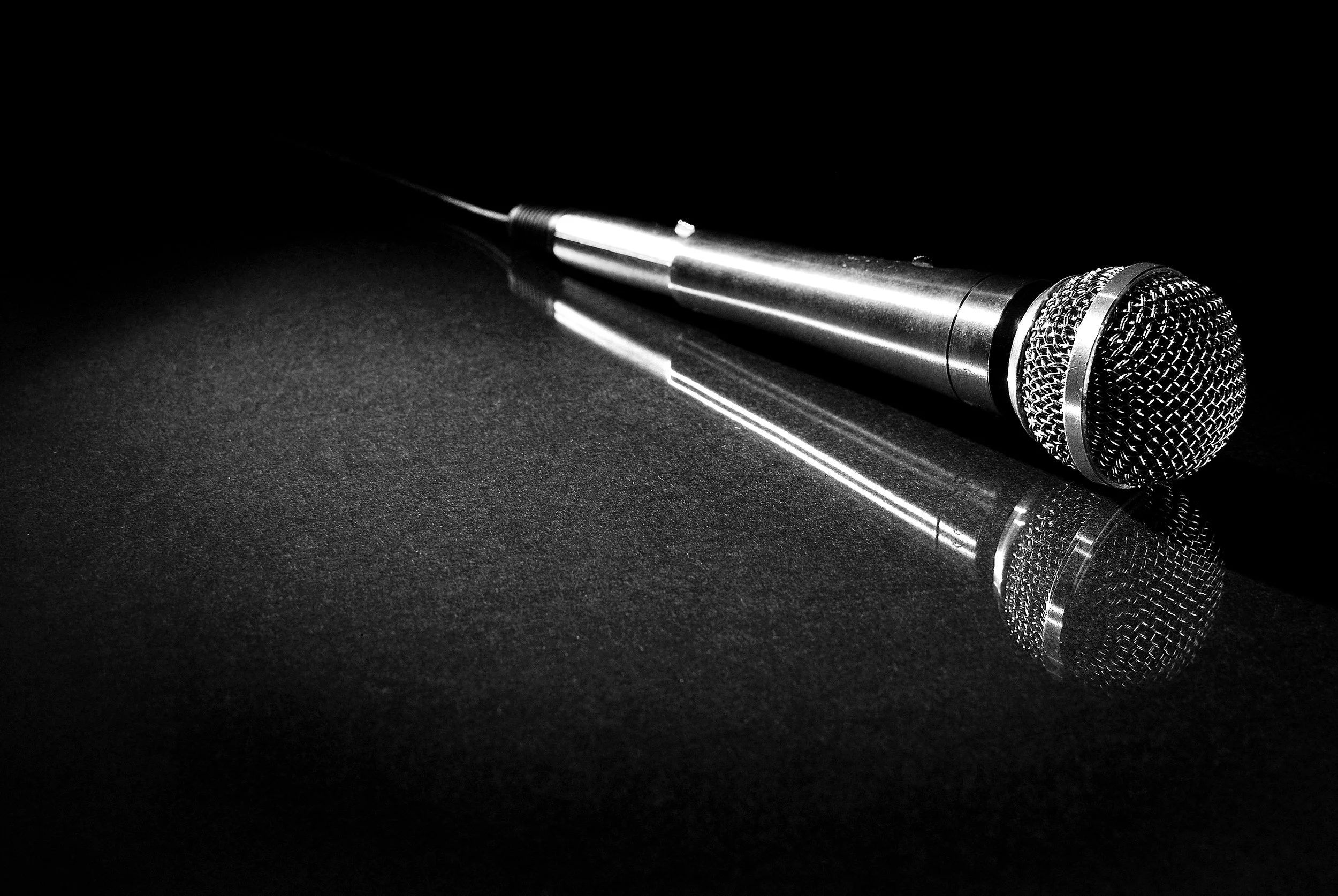 A black and white photo of a microphone lying on a reflective surface with a dark background.
