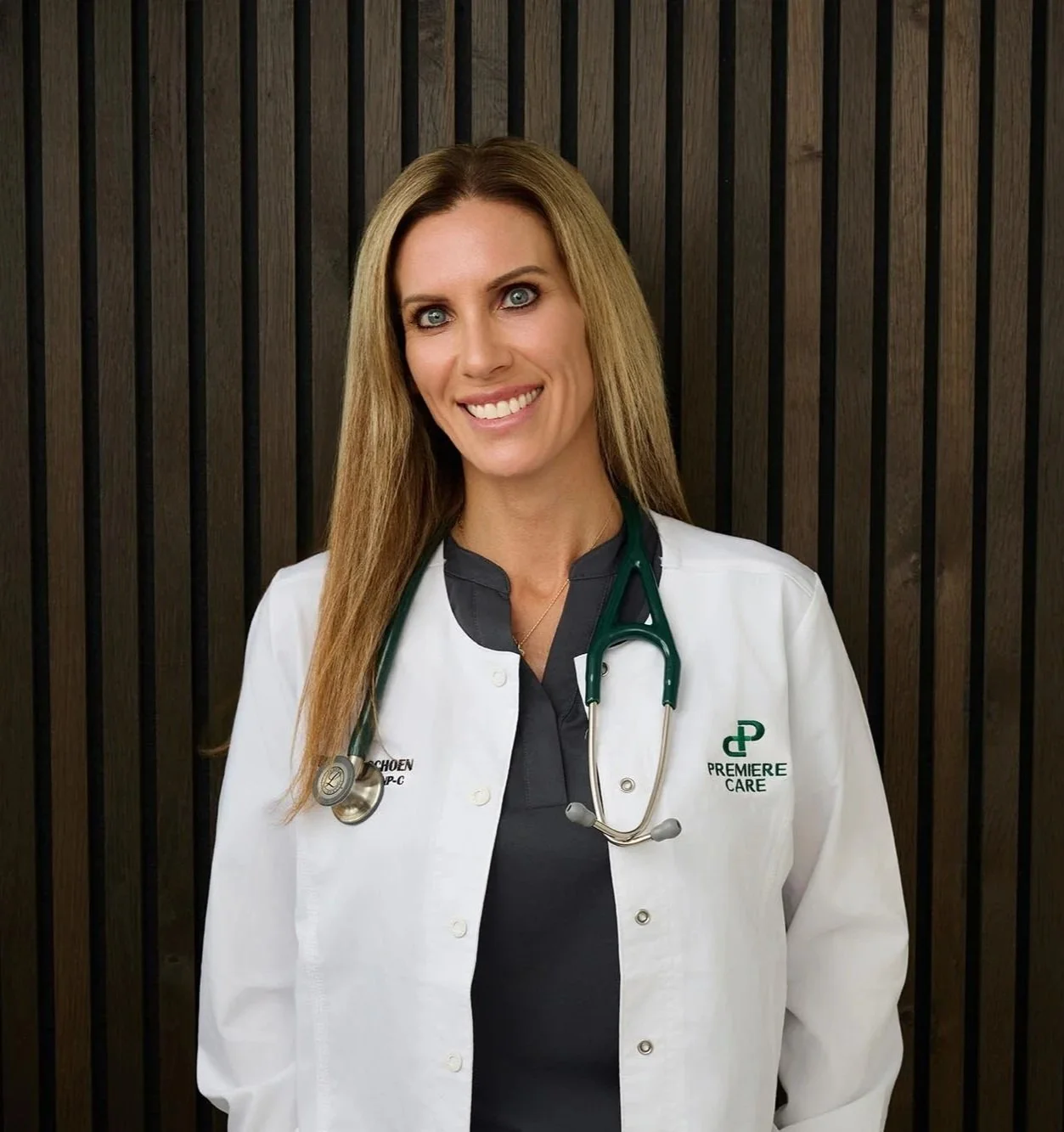 Tiffany Schoen in a white lab coat smiling in front of a wooden slatted wall