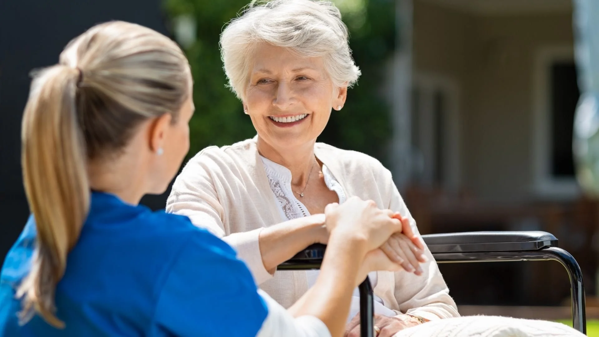 Elderly woman sitting in a wheelchair smiling to a nurse knelt down next to her