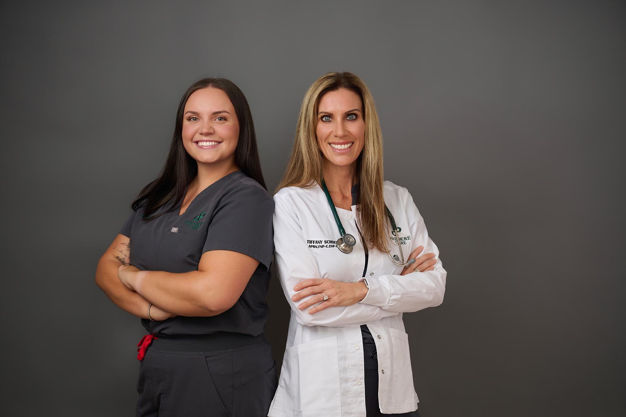 Two Premiere Care nurses with arms crossed standing back to back smiling