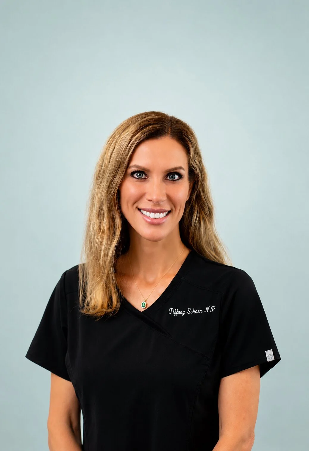 Tiffany Schoen, Nurse Practitioner and Owner of Premiere Care in black scrubs in front of a light blue background