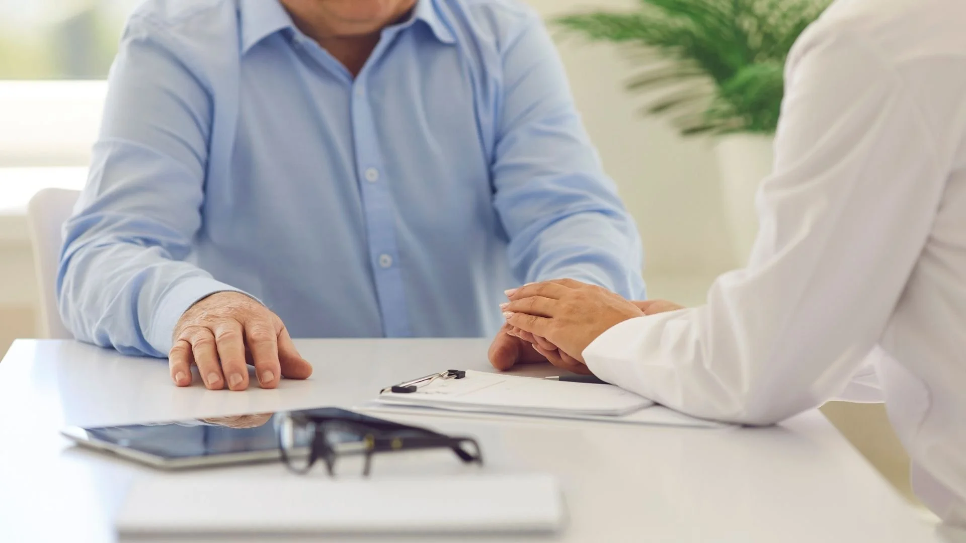 Medical provider touching the hand of an elderly man at a table after reviewing medical plan