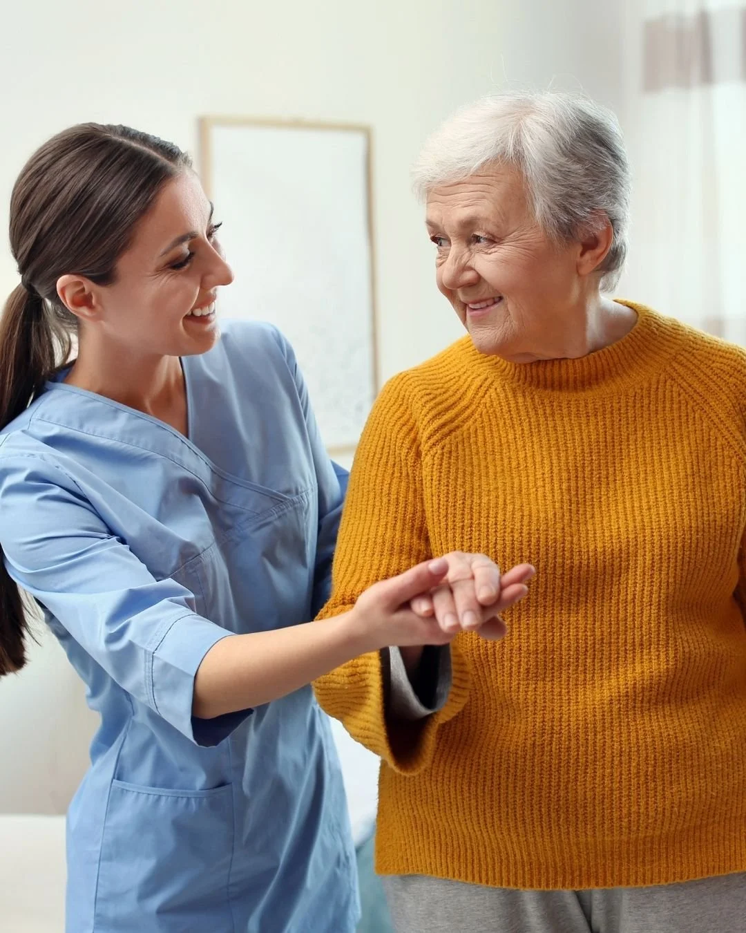 Elderly woman in a yellow sweater smiling as a medical care provider helps her walk