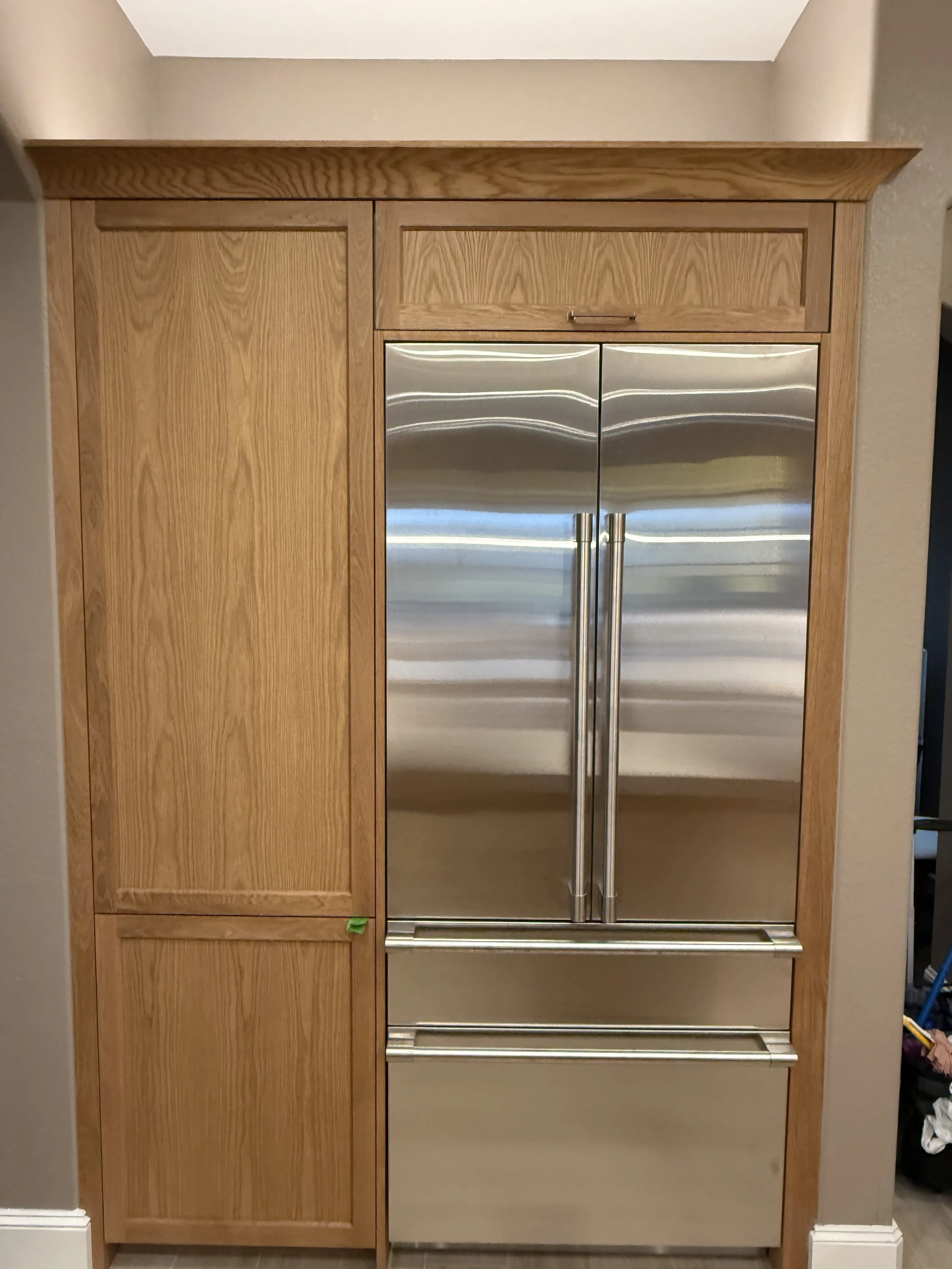 Kitchen cabinet with wood finish and a built-in stainless steel refrigerator with double doors and two drawers below.