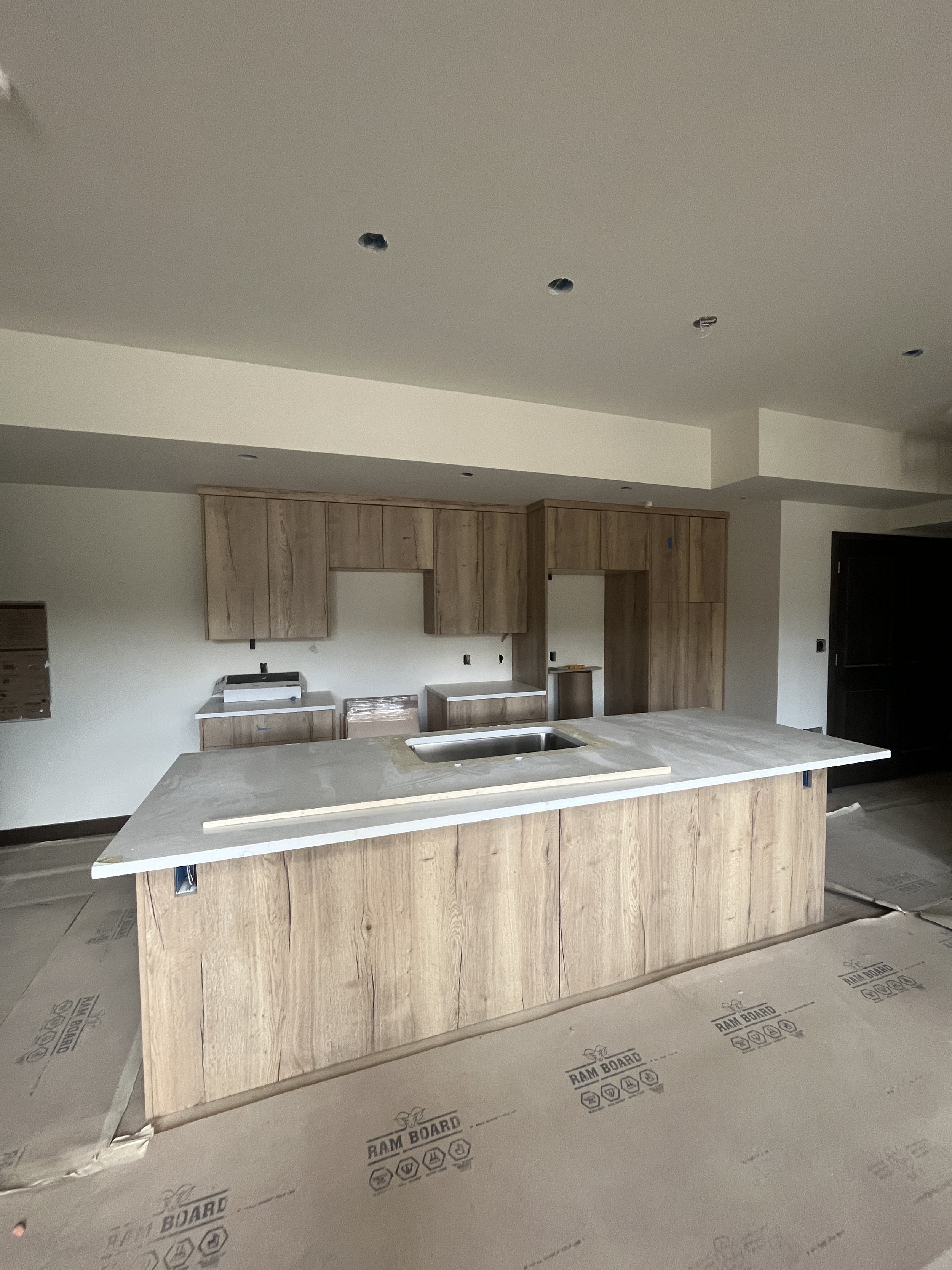 Kitchen under construction with a large central island, wooden cabinets, and an incomplete ceiling with electrical wiring.