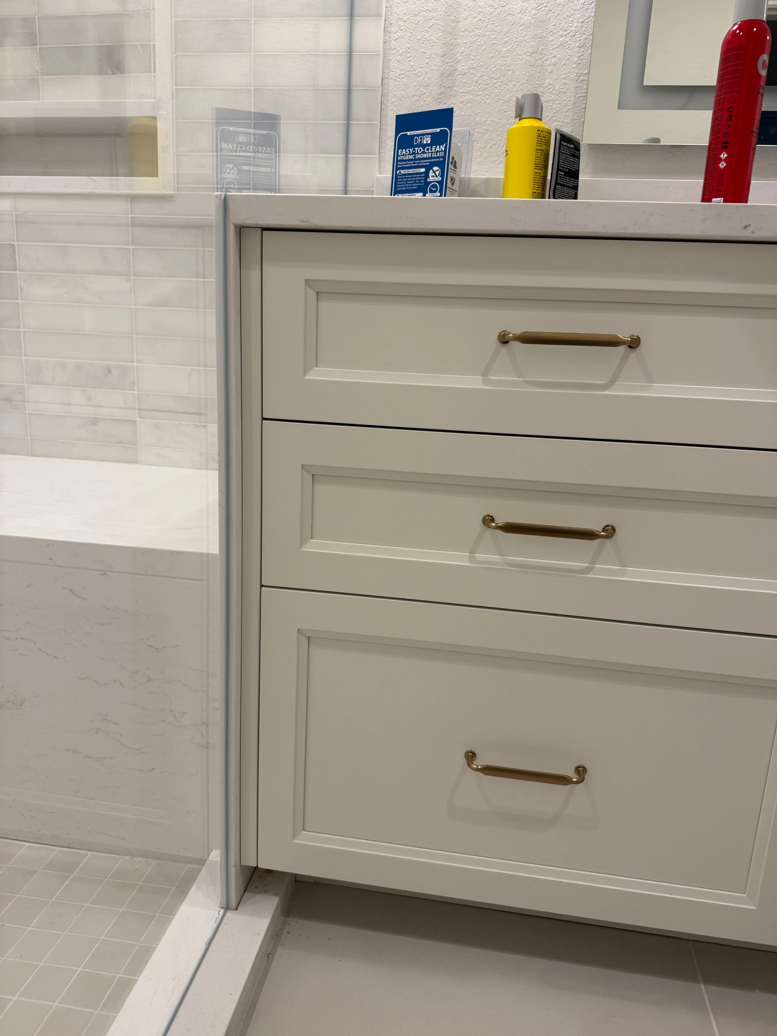 A bathroom countertop with cleaning supplies and a white vanity cabinet with gold handles.