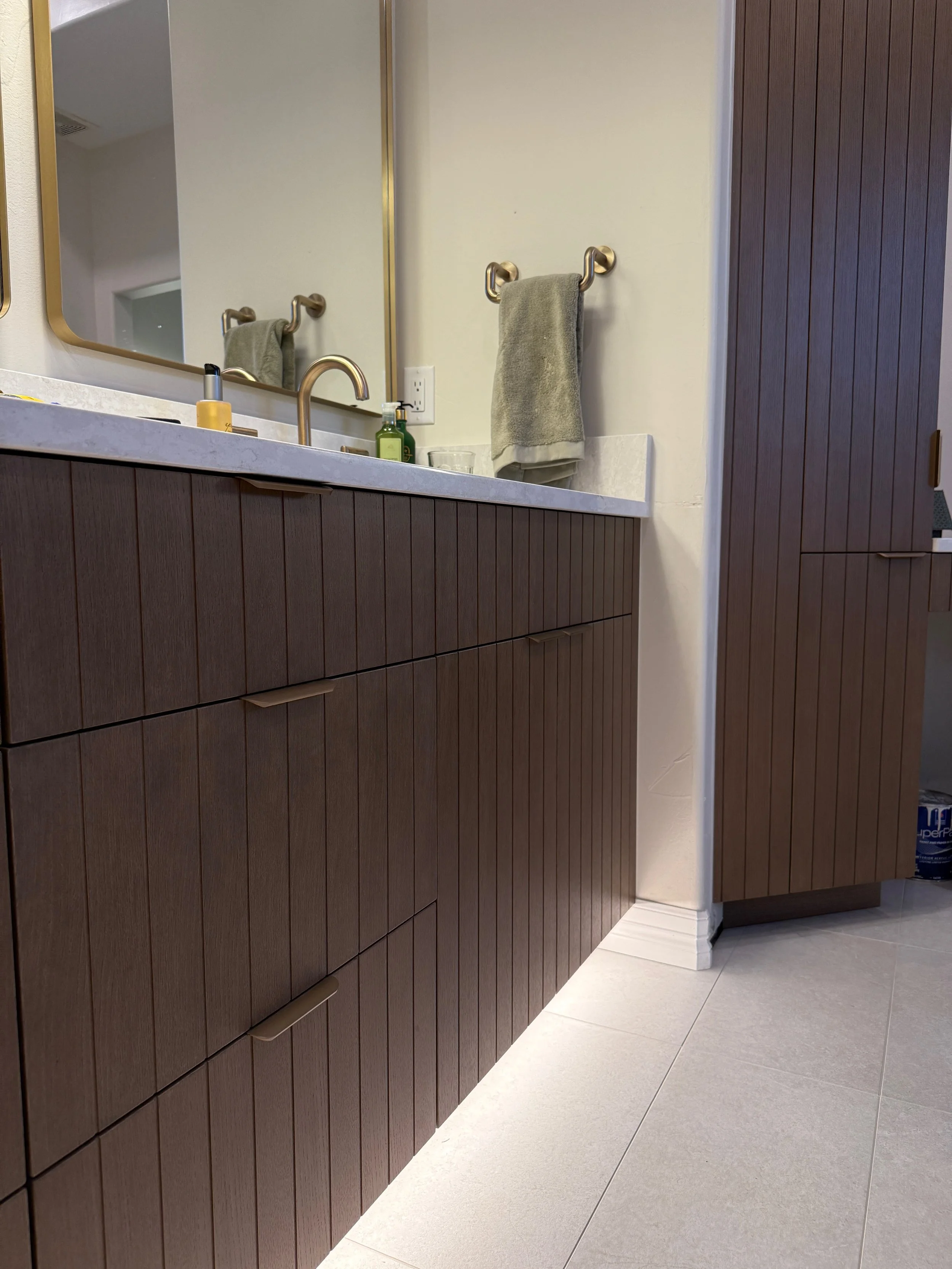Bathroom vanity with a marble countertop, brown wood cabinetry, a mirror, soap dispenser, hand soap, towel, and a cabinet.