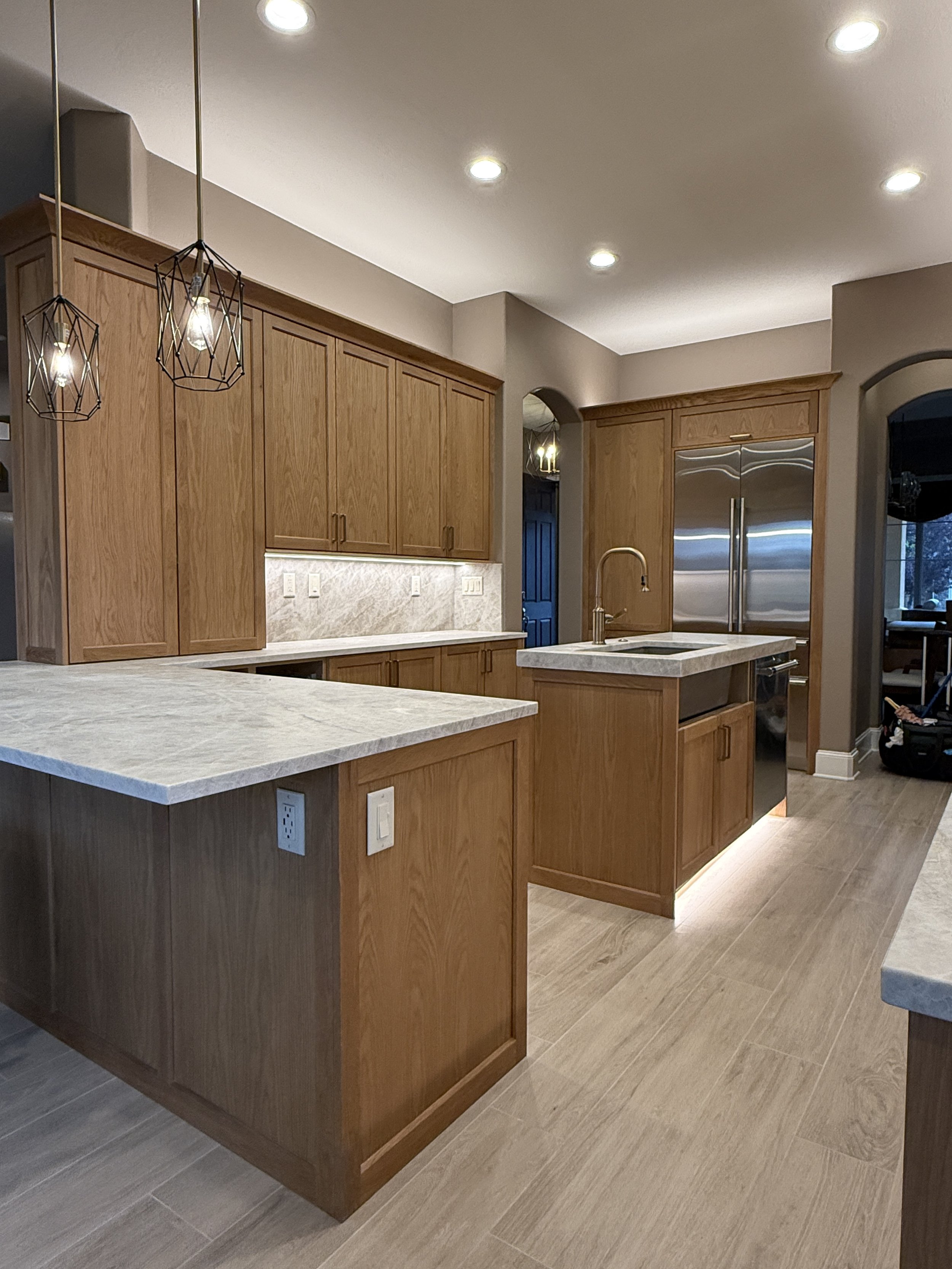 Modern kitchen with wooden cabinets, marble countertops, stainless steel appliances, pendant lighting, and hardwood flooring.