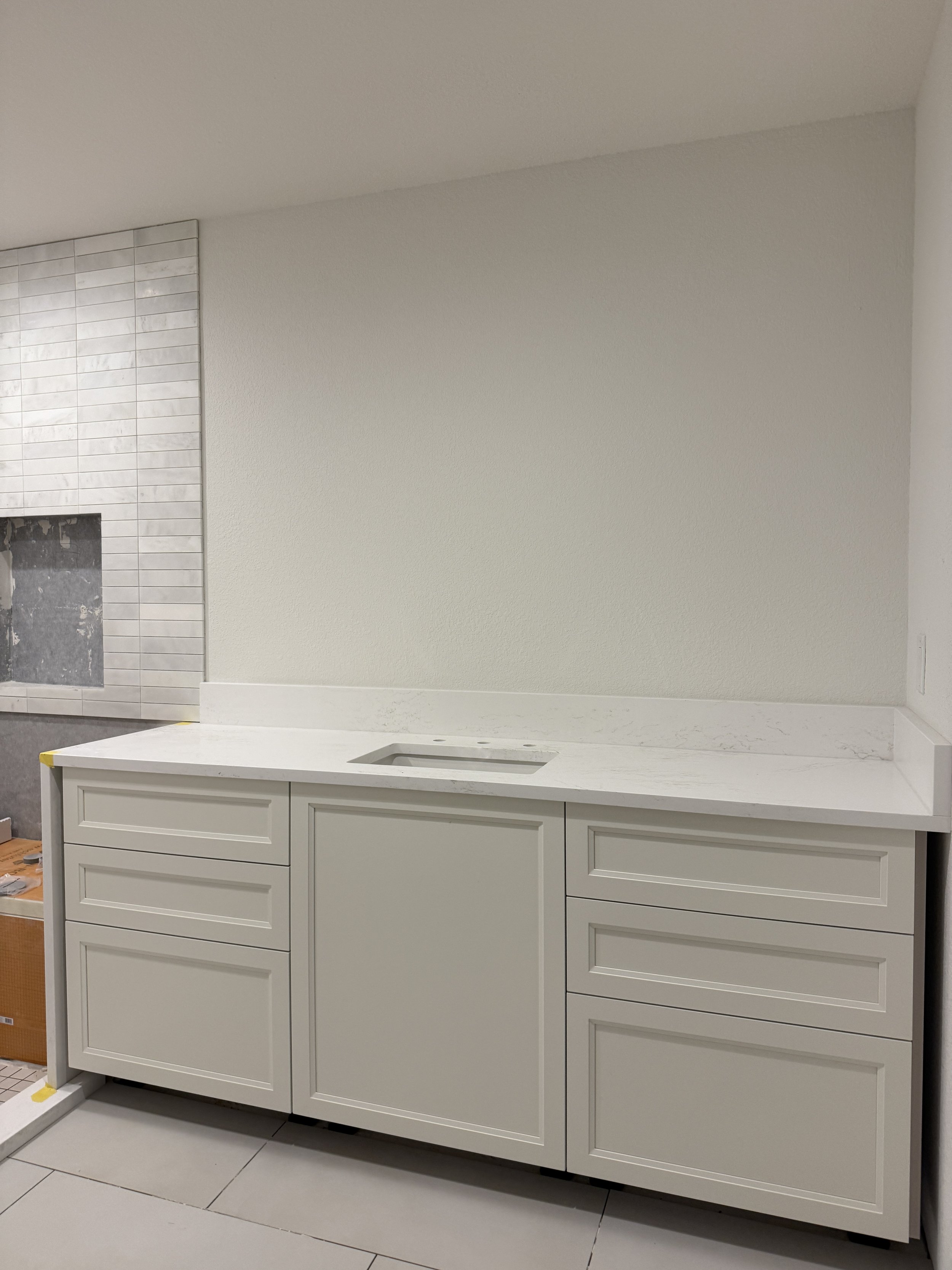 White kitchen cabinet with a marble countertop and a sink, in a modern kitchen under construction.
