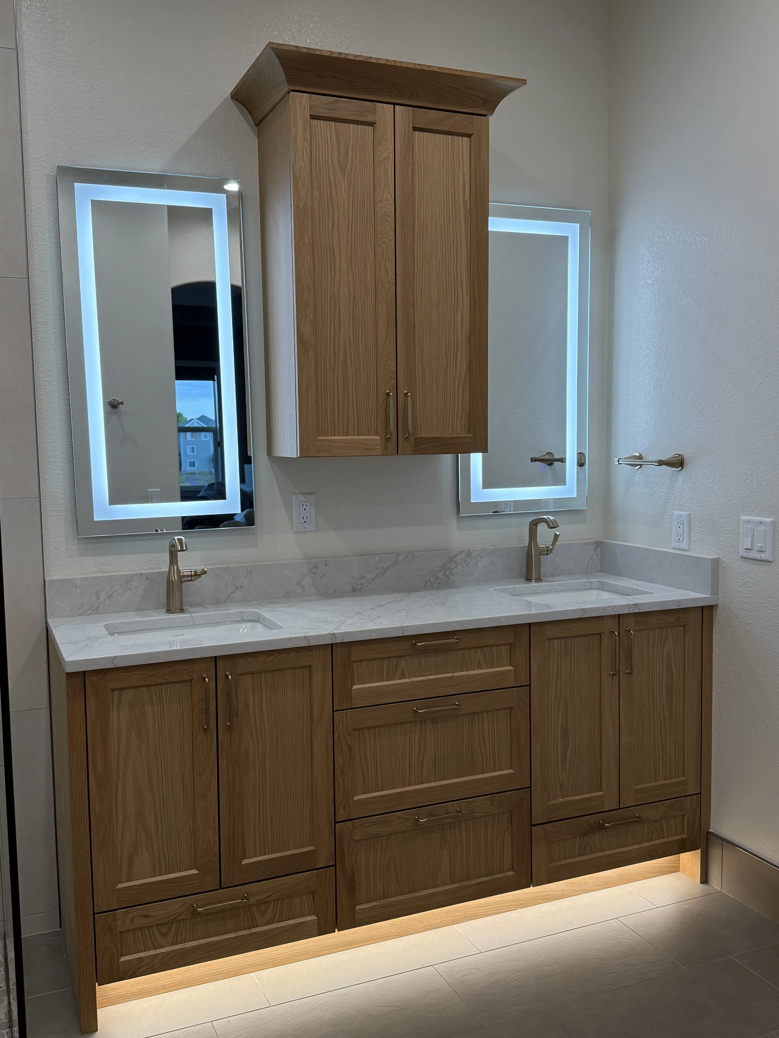 A modern bathroom double vanity with wooden cabinets, a marble countertop, and two illuminated rectangular mirrors.