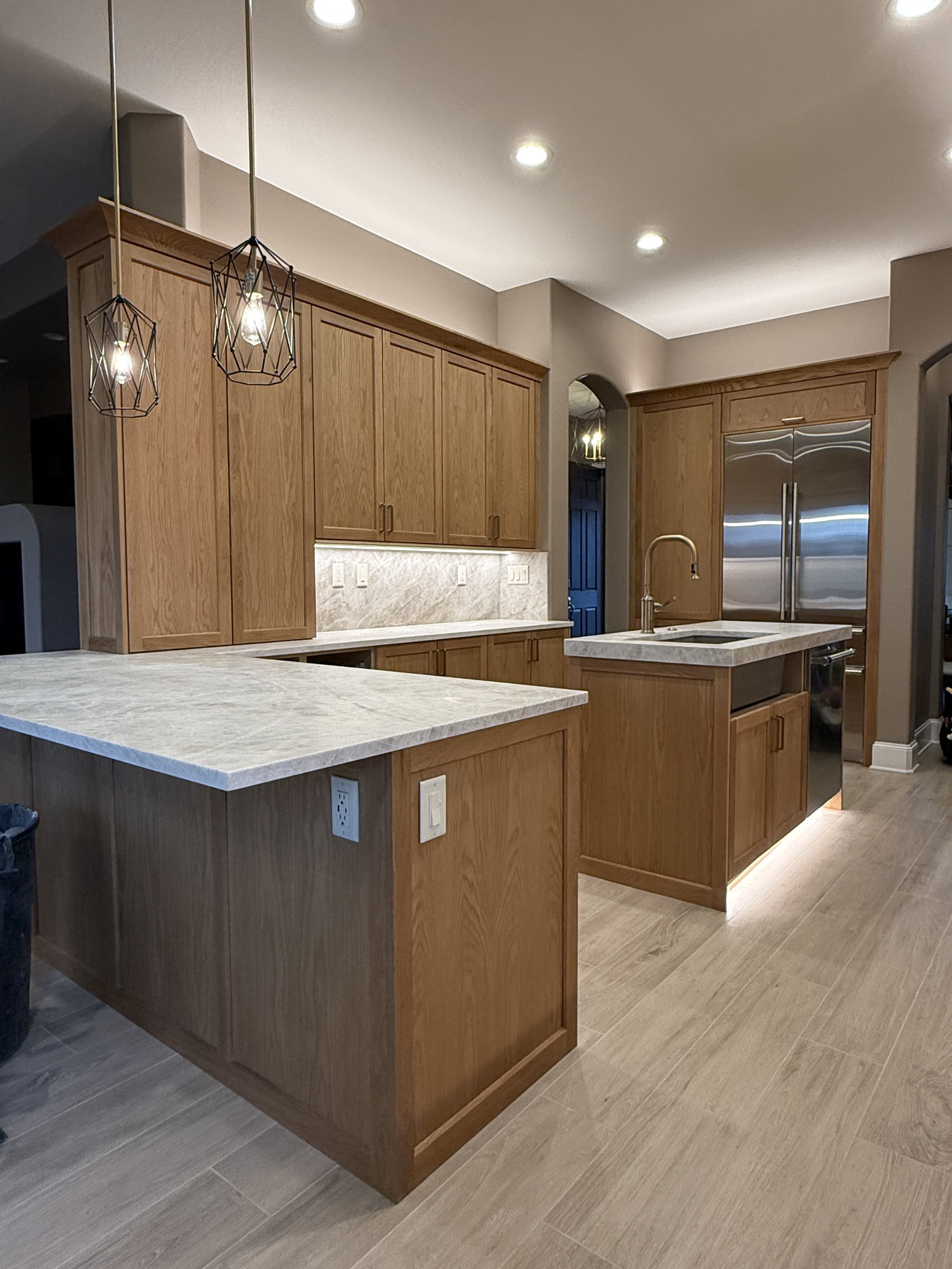 Modern kitchen with wooden cabinets, granite countertops, stainless steel refrigerator, and pendant lighting.