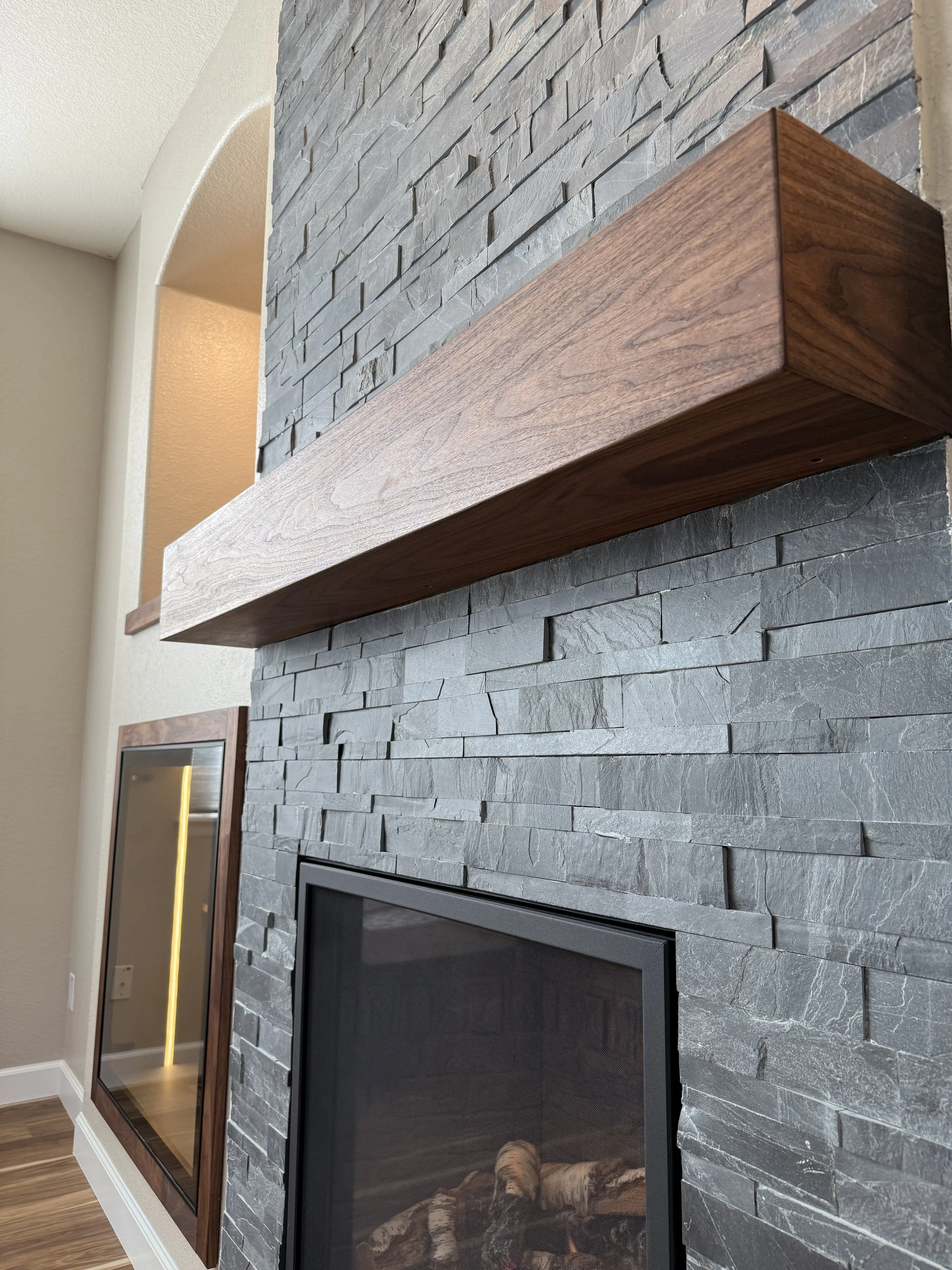 Close-up of a modern living room fireplace with a gray stone surround and a wooden mantel.