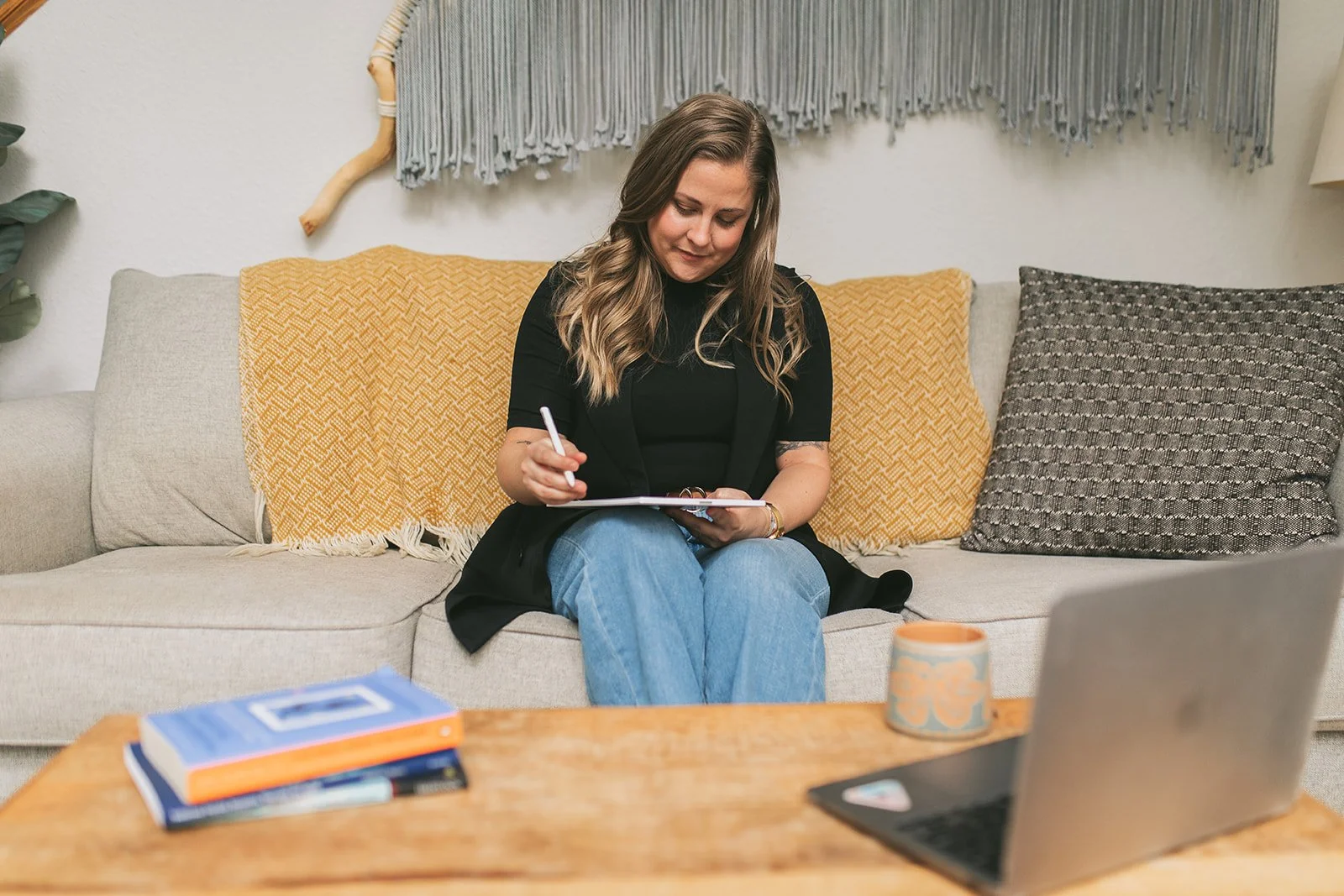 Meredith Garreau writing notes on a clipboard in her home office, with a laptop and clinical books on the coffee table in front of her