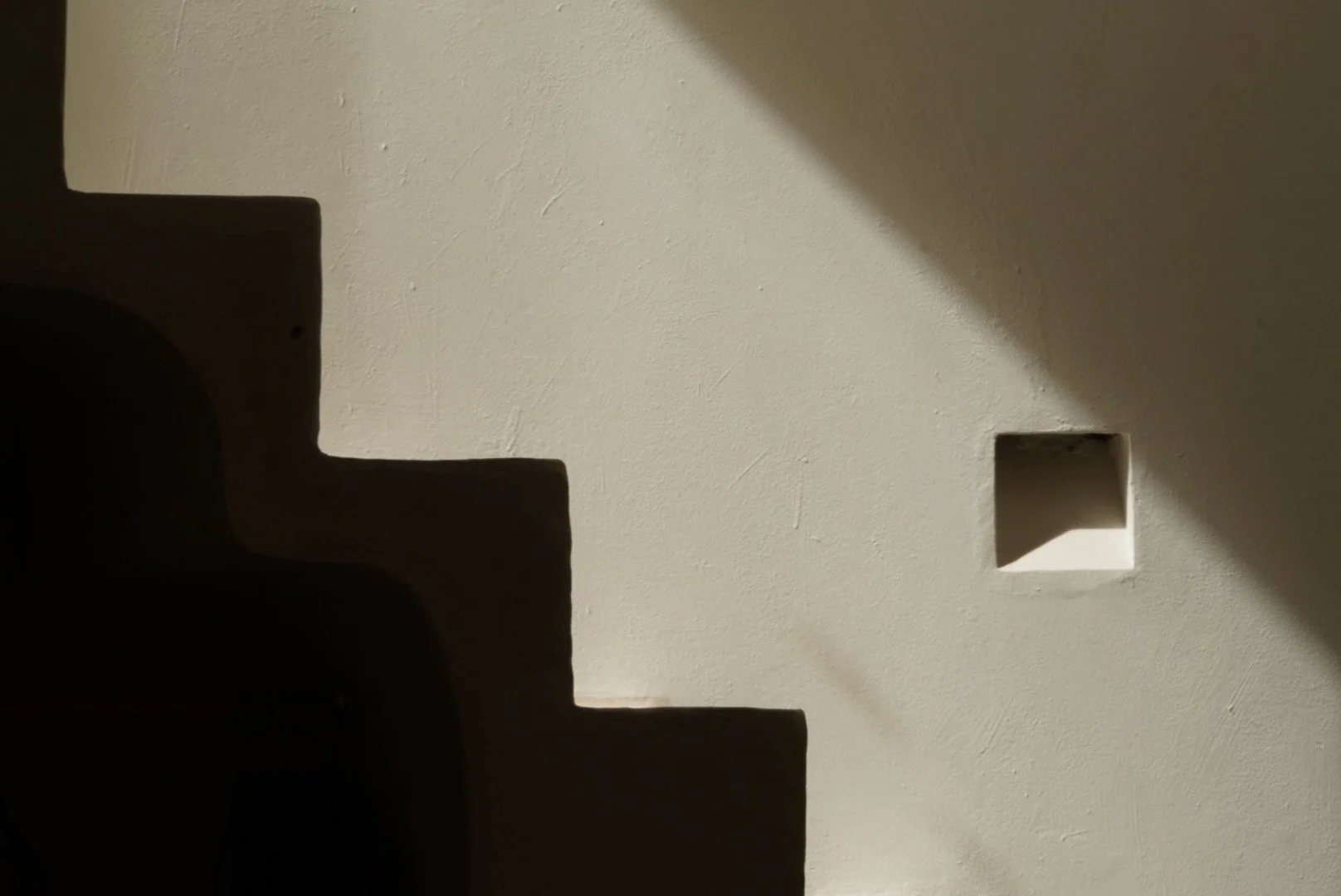 Minimalist photograph of staircase shadows and light on a white wall, suggesting forward movement, transition, and quiet clarity