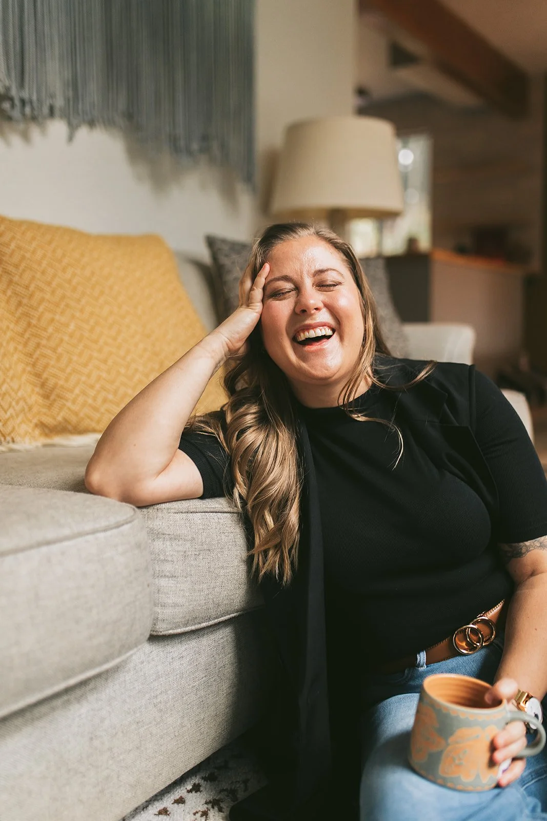 Meredith Garreau, IFS therapist and founder of Wanderwell Counseling, laughing warmly while holding a mug on a couch