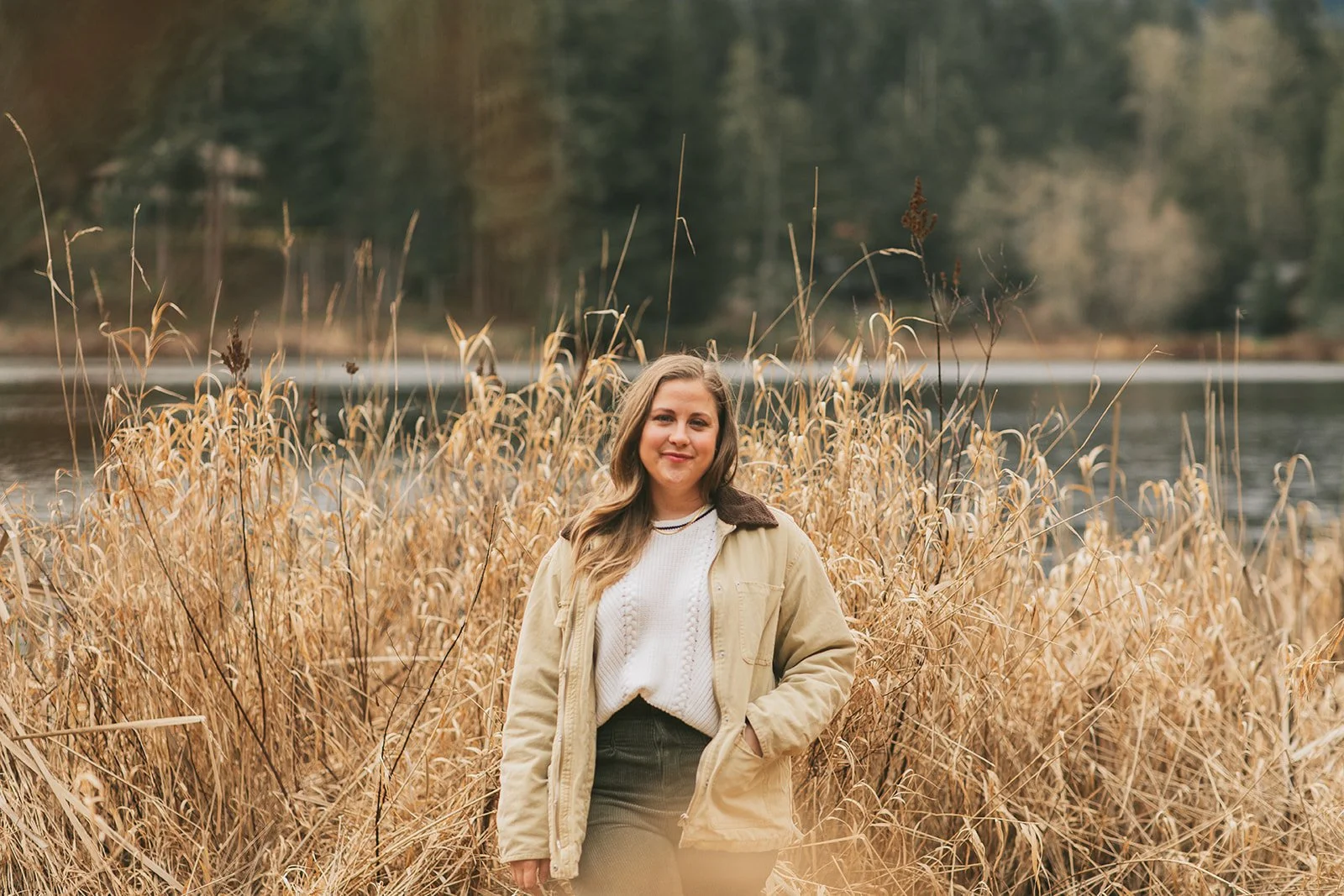 Meredith Garreau, founder of Wanderwell Counseling, standing among tall golden grasses at a lakeside with evergreen trees in the background