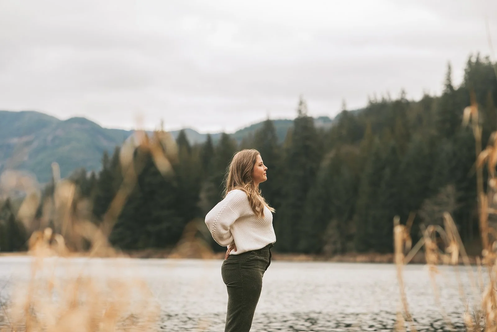 Meredith Garreau standing in profile at a lakeside with mountains and evergreen trees behind her, looking thoughtfully into the distance