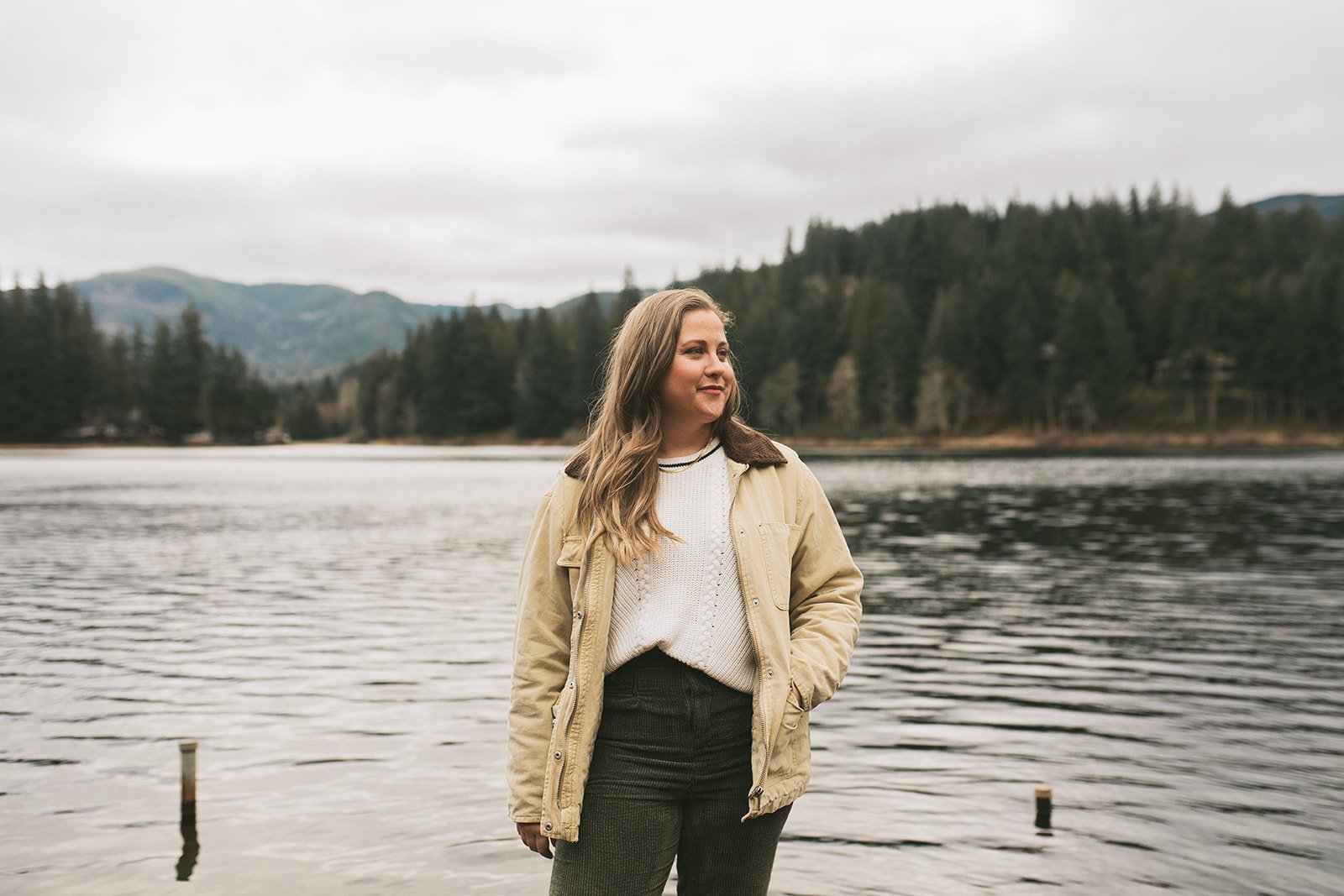 Meredith Garreau, founder of Wanderwell Counseling, standing at the edge of a lake looking into the distance, with mountains and evergreen forest behind her
