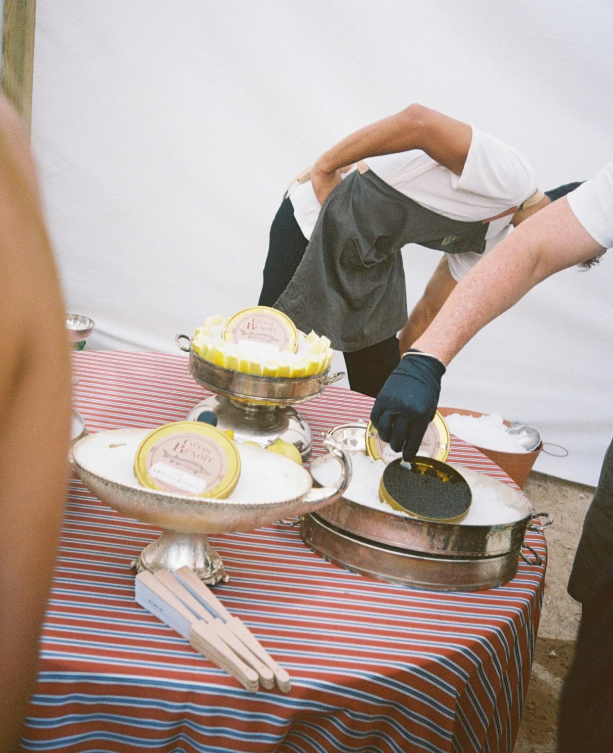People serving lemon-themed desserts from silver trays on a striped tablecloth at an event.