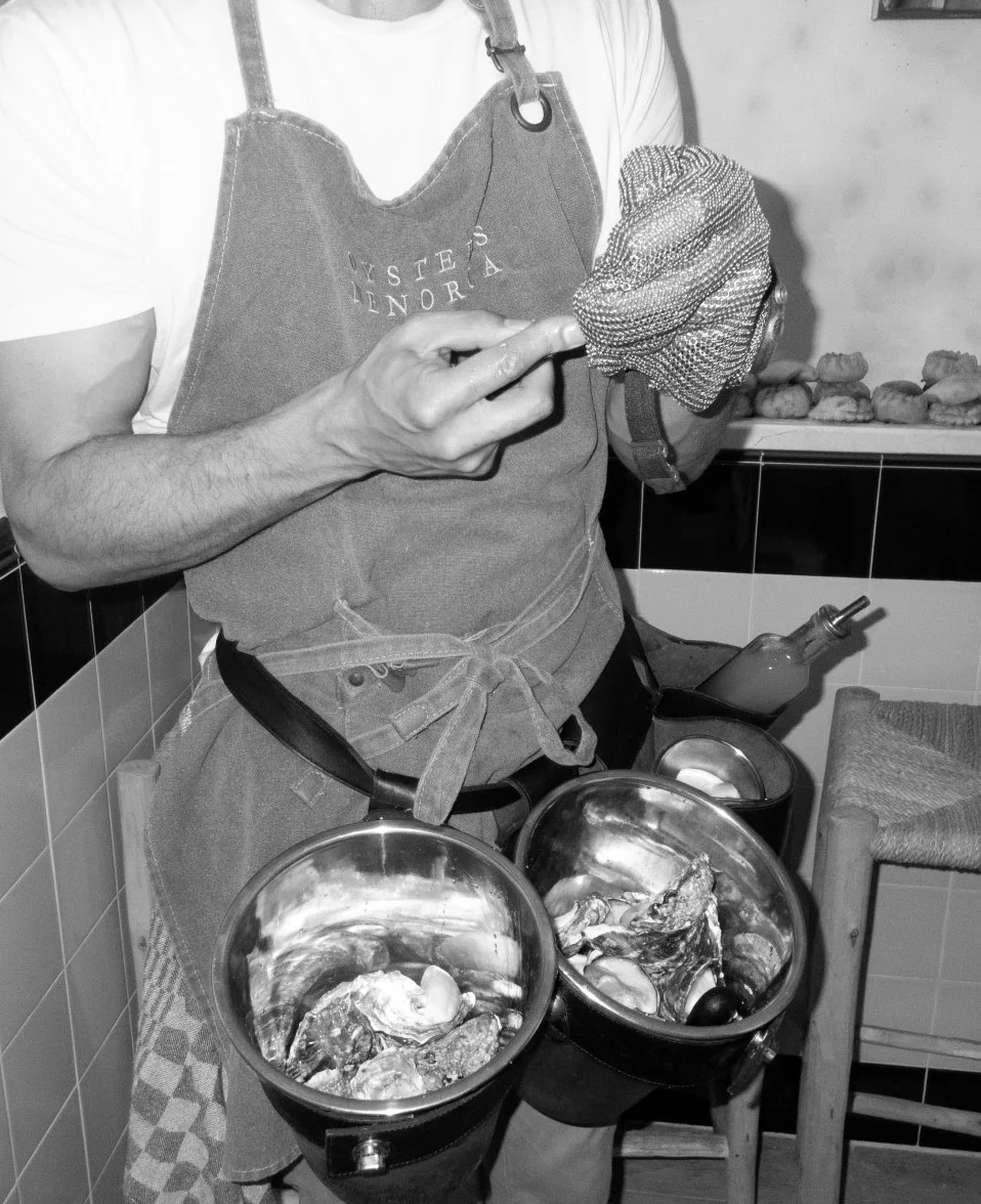 Person wearing an apron preparing seafood, using a toothpick to handle fish or shellfish, with bowls of seafood on a table.