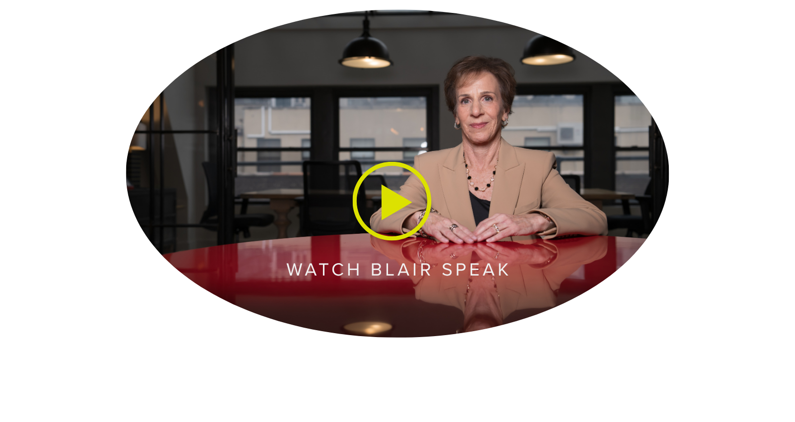 Thumbnail image of an older woman with short hair wearing a beige blazer, sitting at a red desk in a modern office space with large windows and black chairs in the background, with overlay text "Watch Blair Speak".