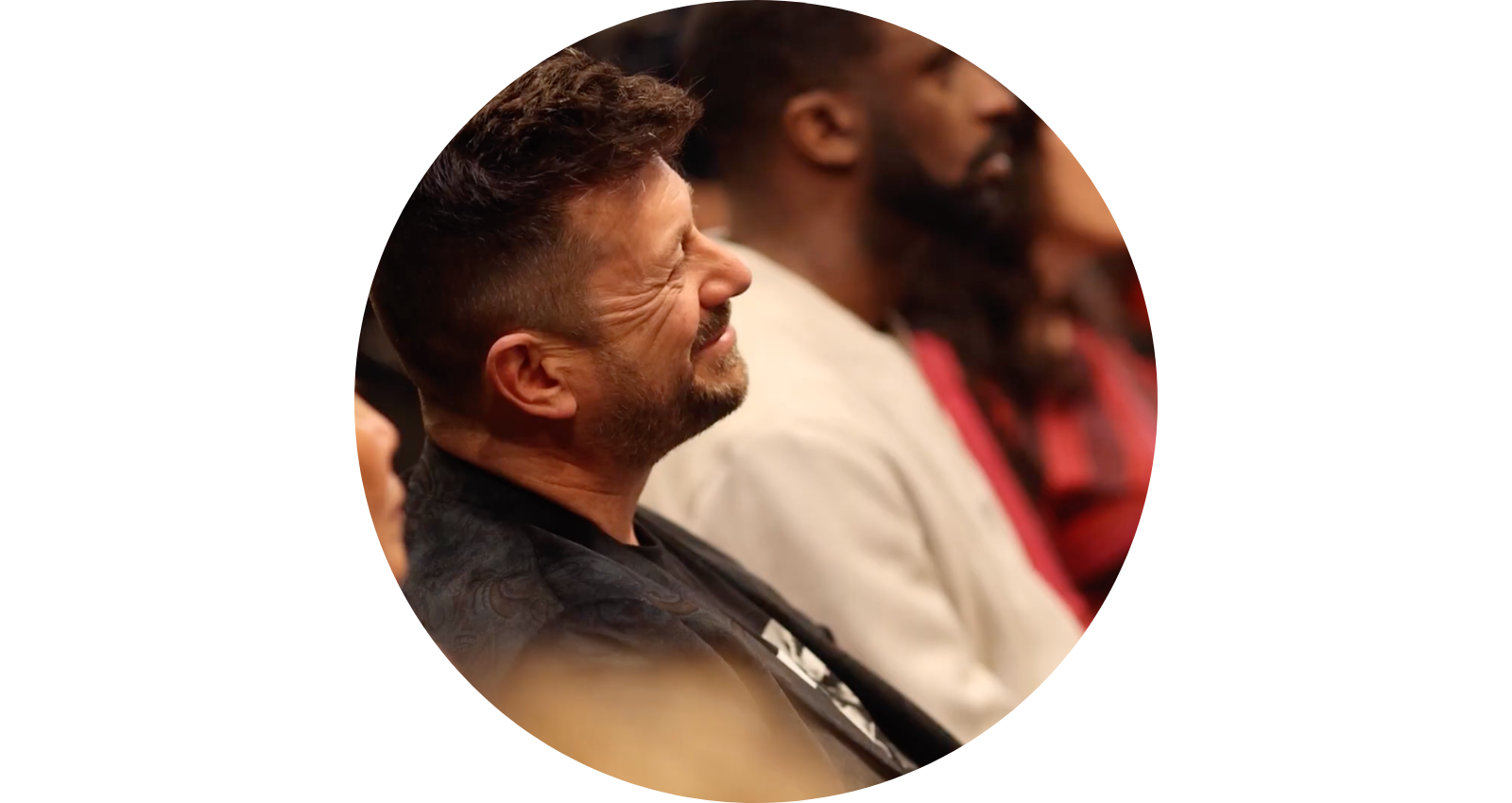 People sitting in a row, attentively listening, with the man in the foreground smiling and the others focused.