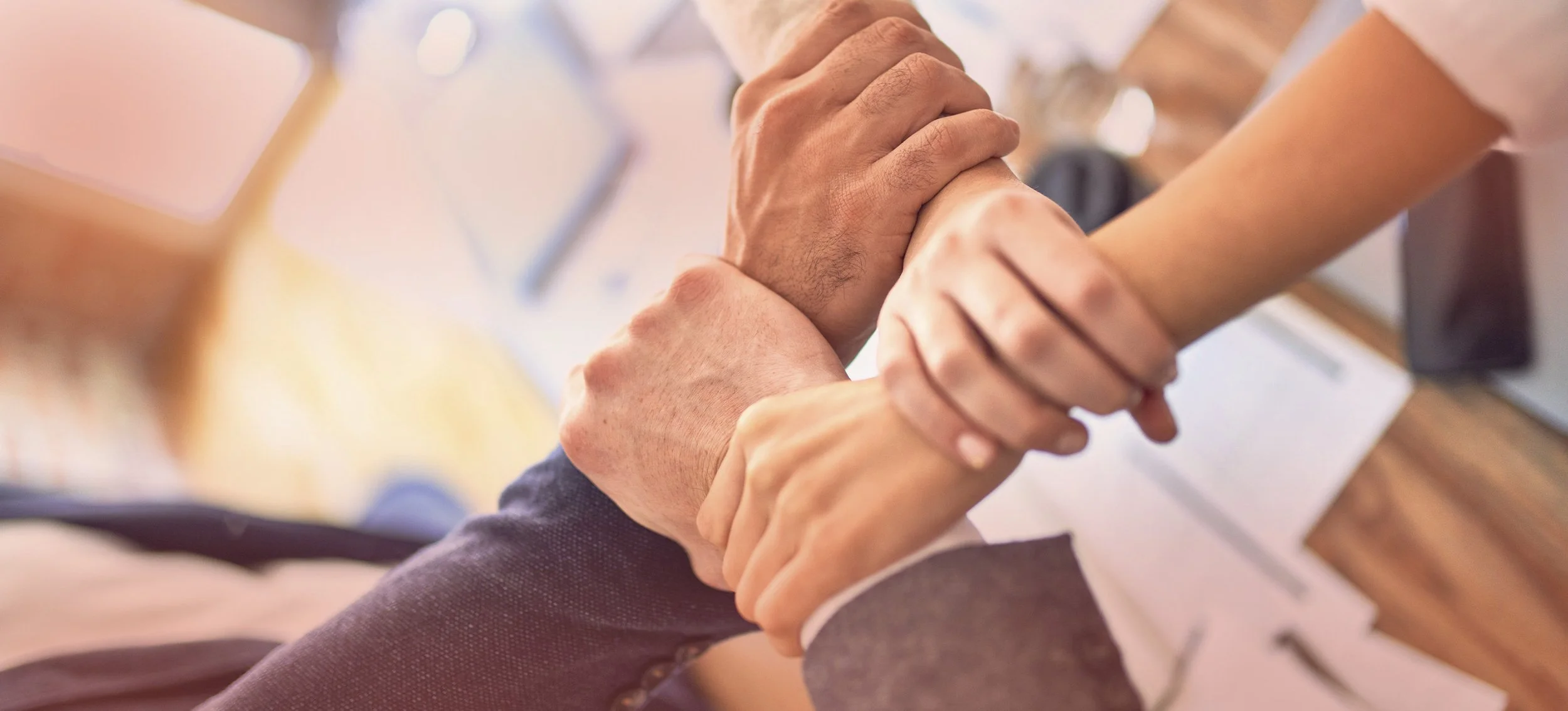 Close-up of two people clasping hands in partnership or teamwork, possibly during a meeting or conference.