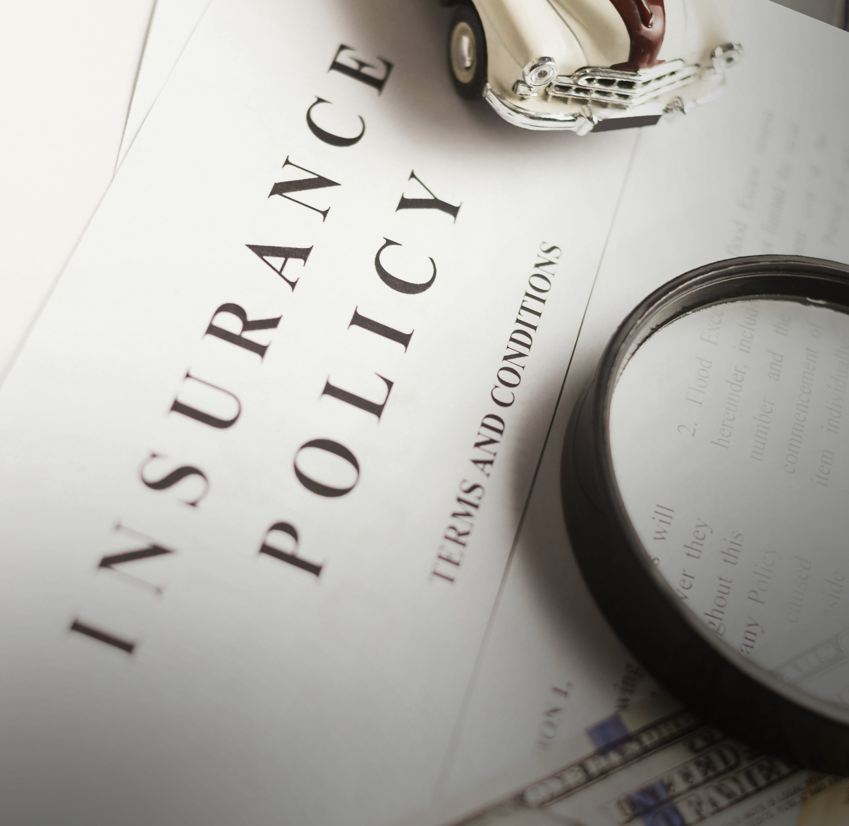 A survey and policies document with a toy vintage car on top, a magnifying glass partially visible, and a financial document below.