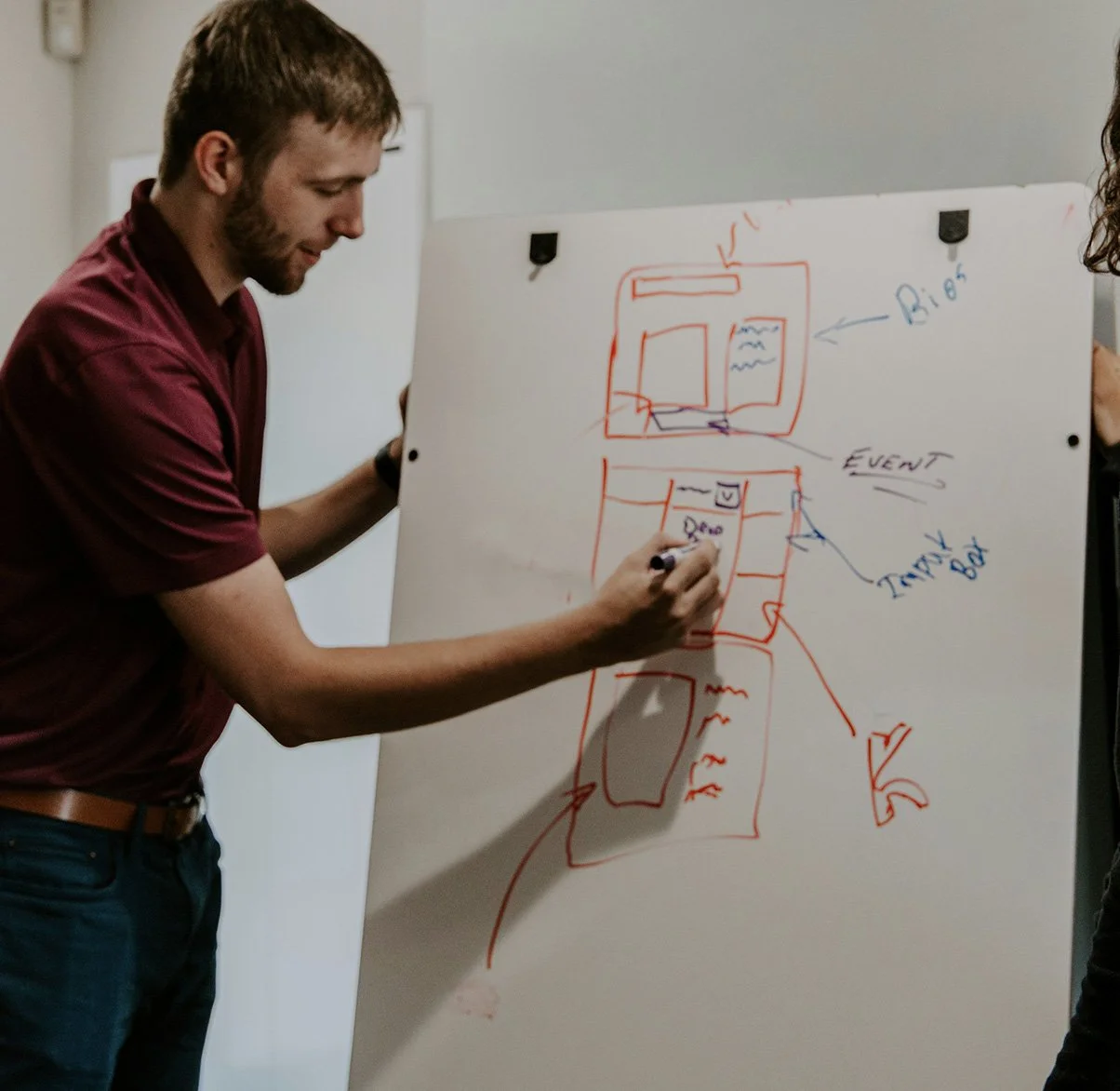 Person in a maroon shirt drawing a diagram on a large whiteboard with colorful markers, including boxes labeled 'Big,' 'Event,' and 'Time Box.'