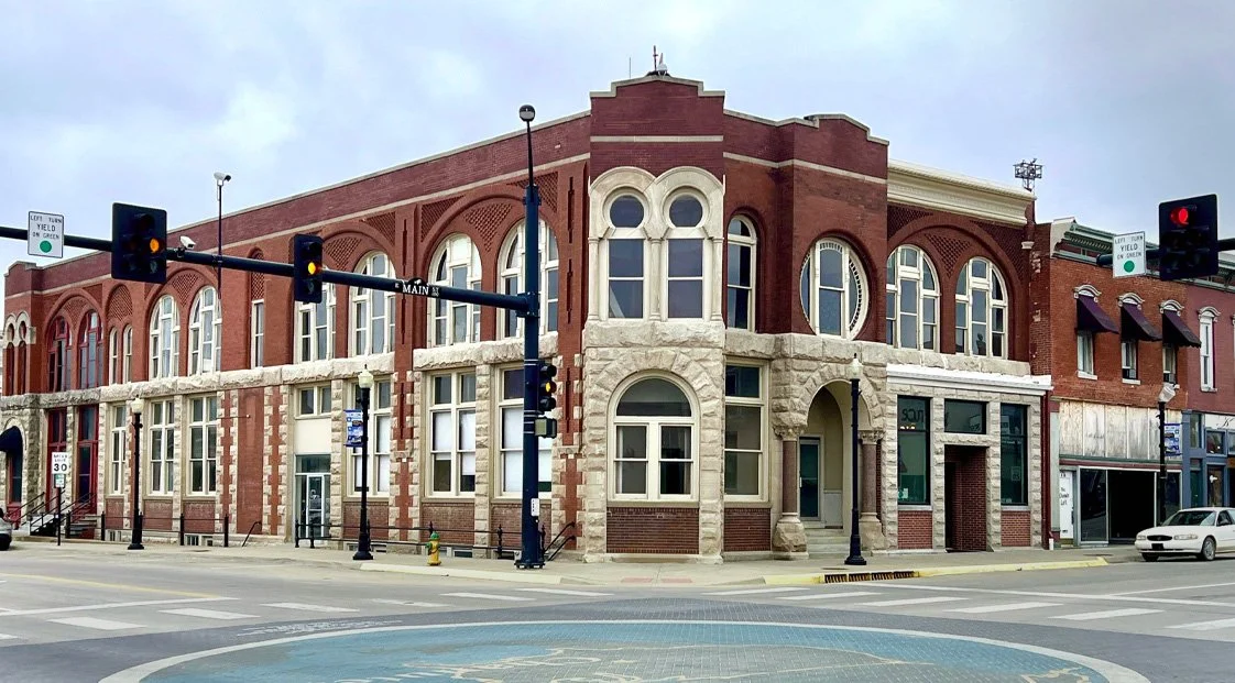 Red brick historic building at a street corner with traffic lights and crosswalks.