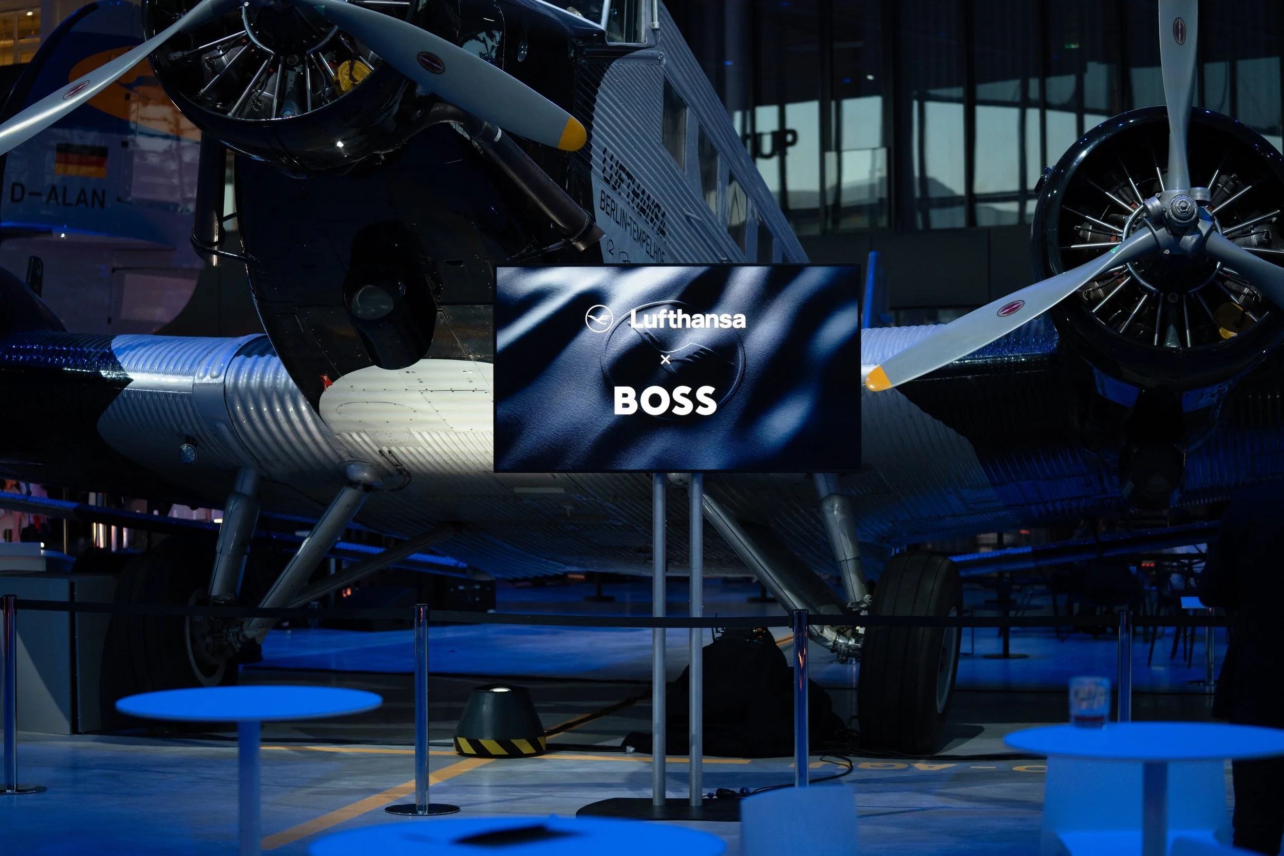 Bild von dem Event des Releases der neuen Lufthansa Dienstkleidung 2026: Ein Flugzeug mit einem Bildschirm davor, auf dem steht "Lufthansa x BOSS"