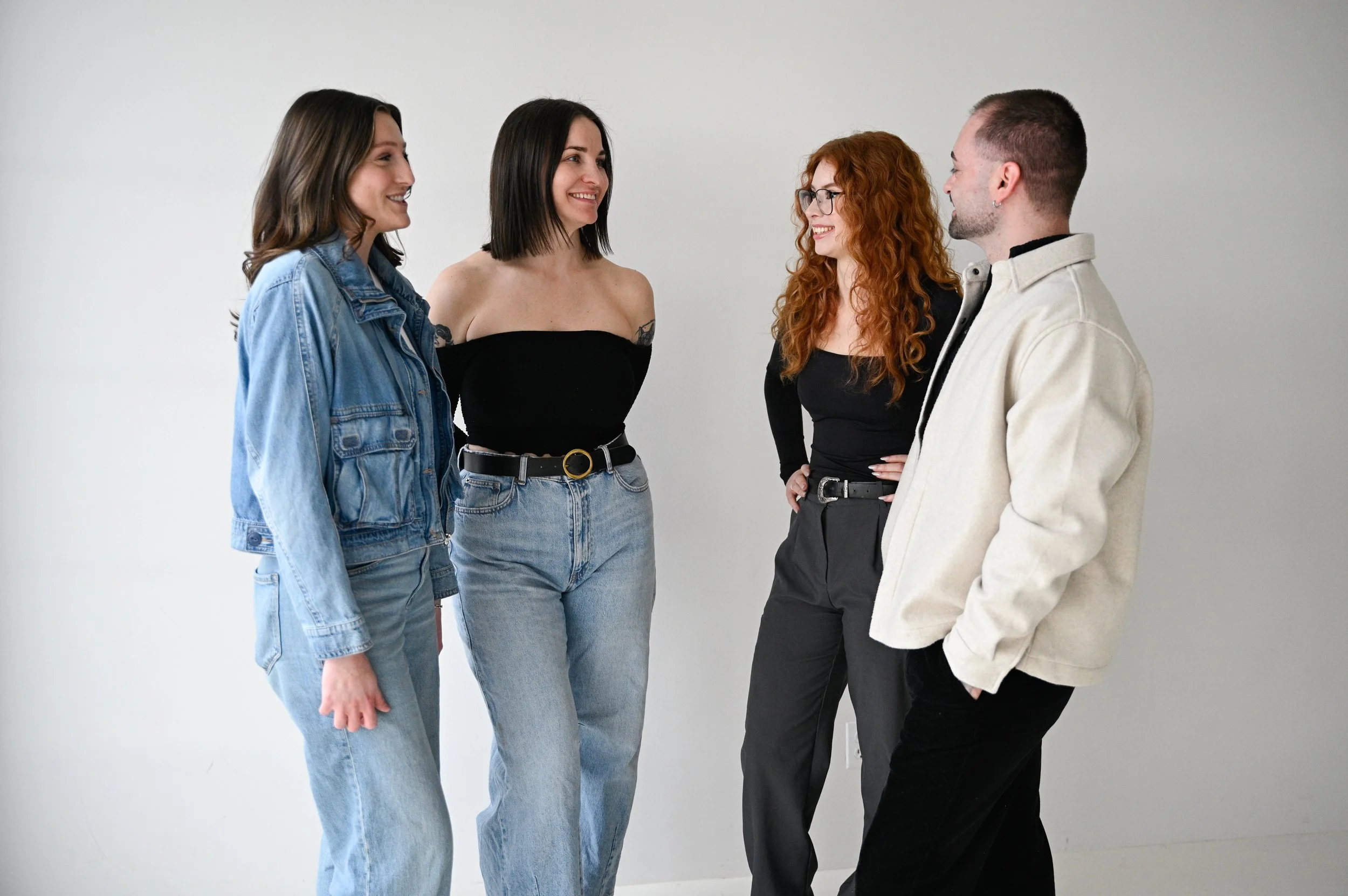 Four young adults standing in a row, smiling, and talking to each other against a plain white background.