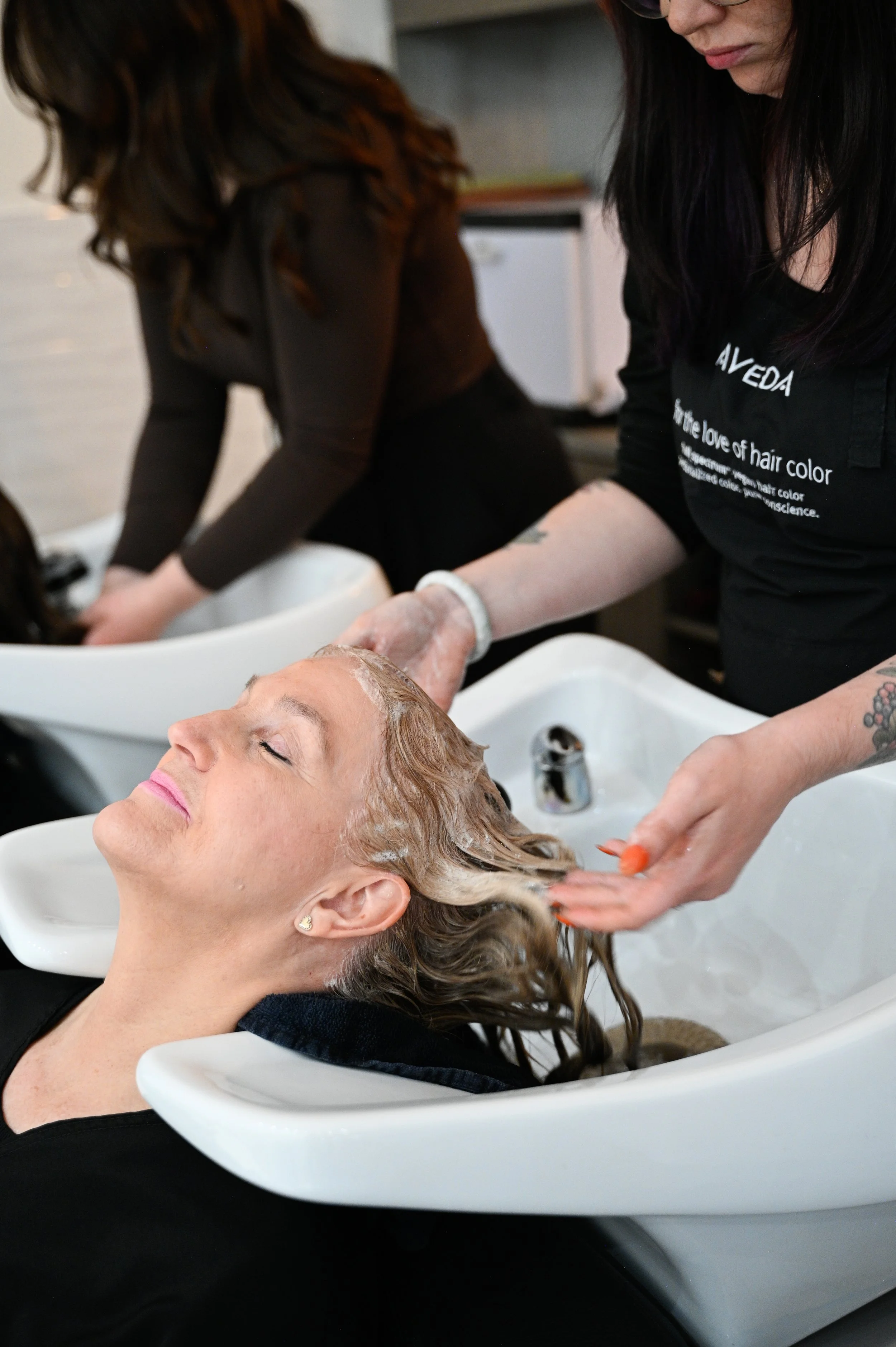 A woman relaxing with her eyes closed while getting her hair washed by a stylist at a salon.