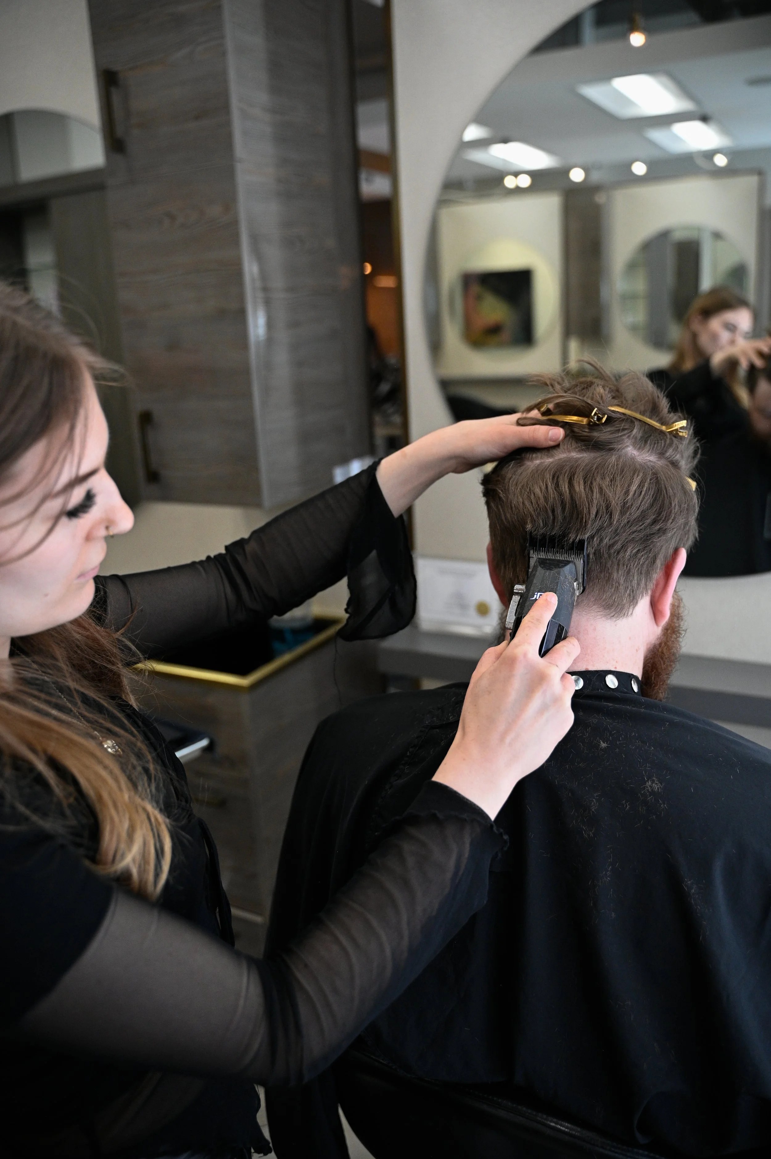 Hairdresser cutting a man's hair with clippers in a salon.