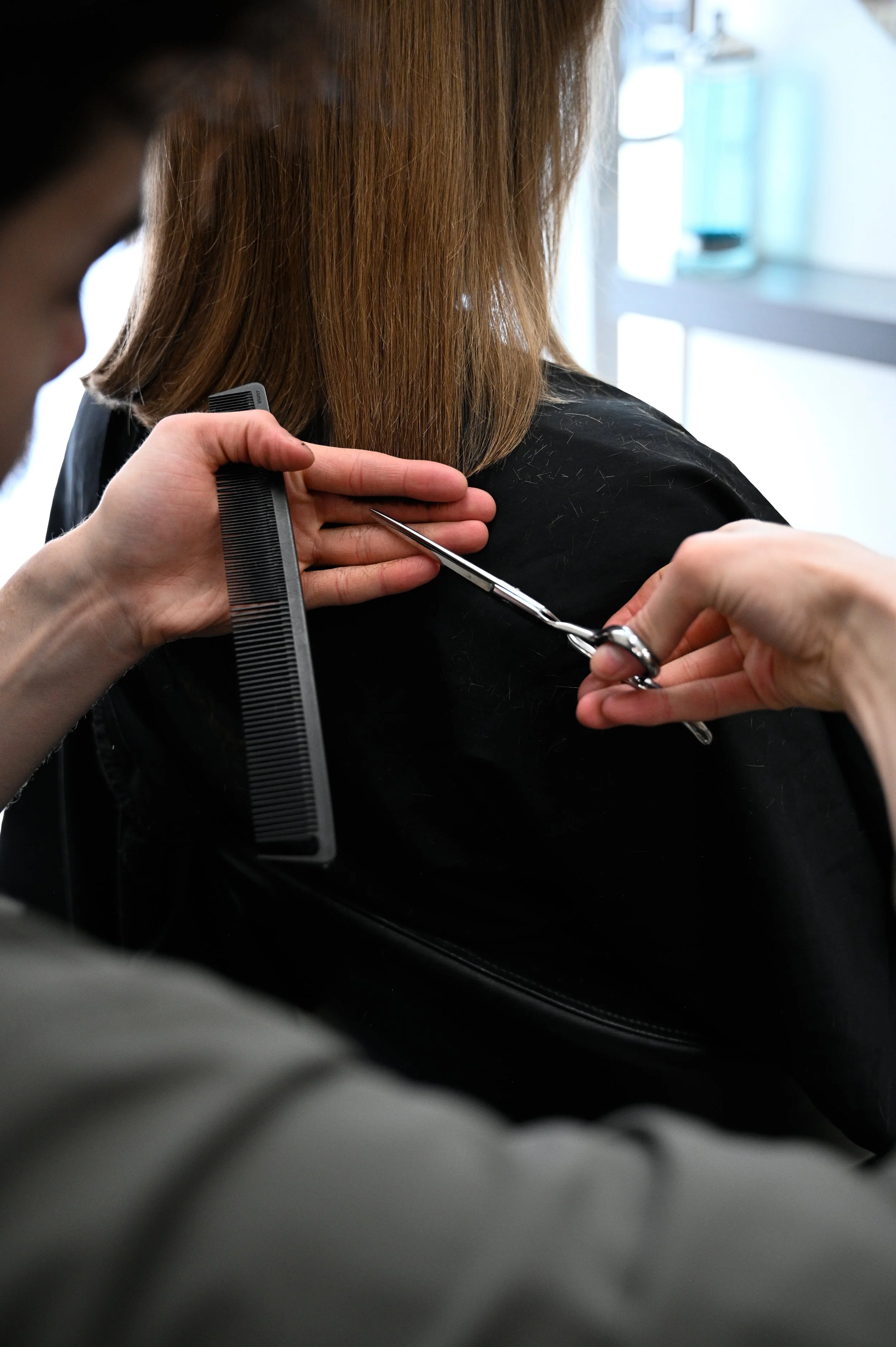 A hairstylist cutting a woman's hair with scissors while holding a comb, in a salon.