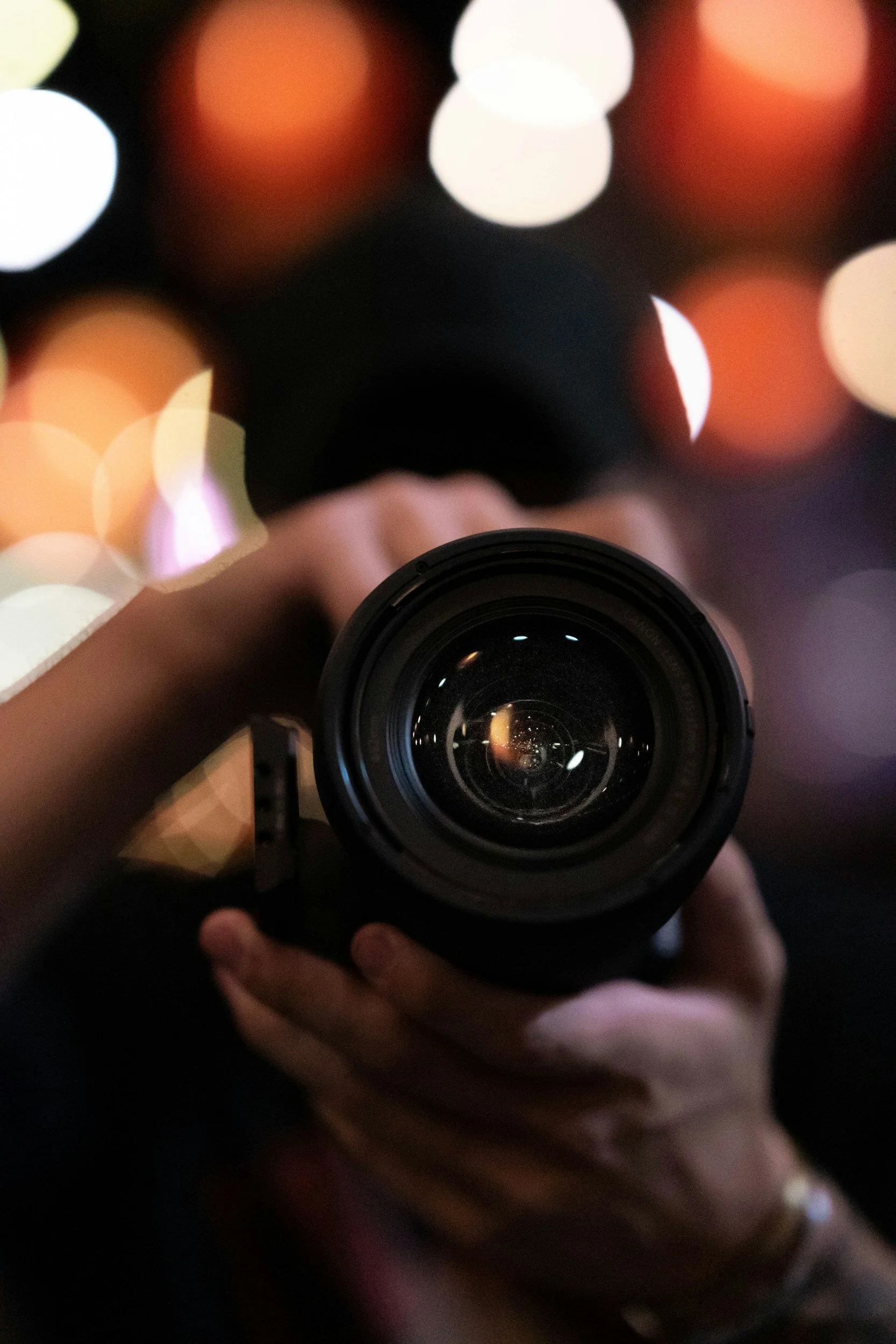 A person holding a camera with blurred colorful lights in the background.