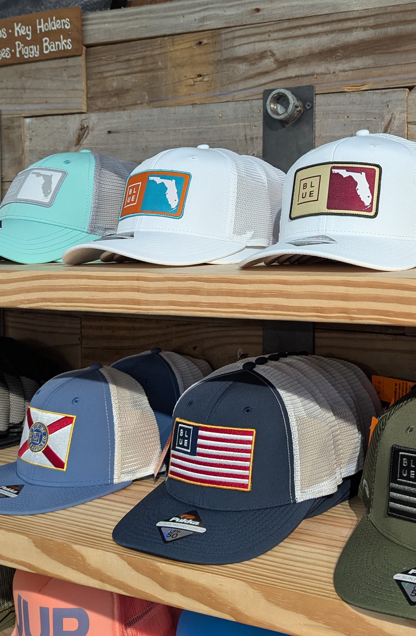 Various baseball caps with patches of Florida state flag, Florida outline, and American flag, displayed on wooden shelves.