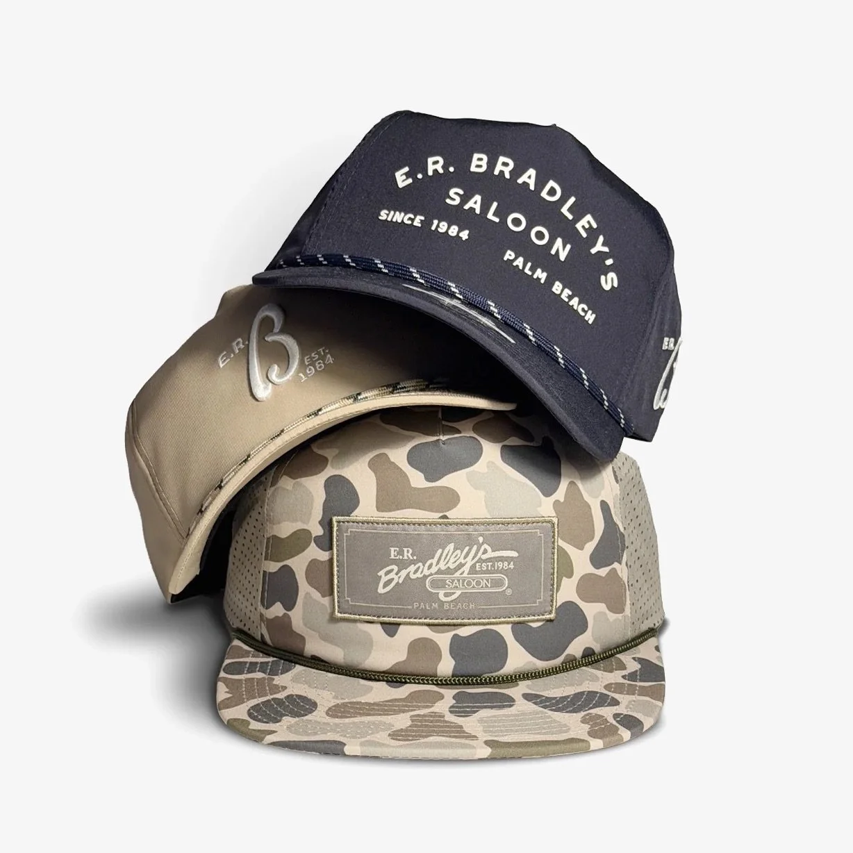 Three baseball caps stacked, with the top navy, the middle beige, and the bottom camo print, all featuring the "E.R. Bradley's Saloon Palm Beach" logo.