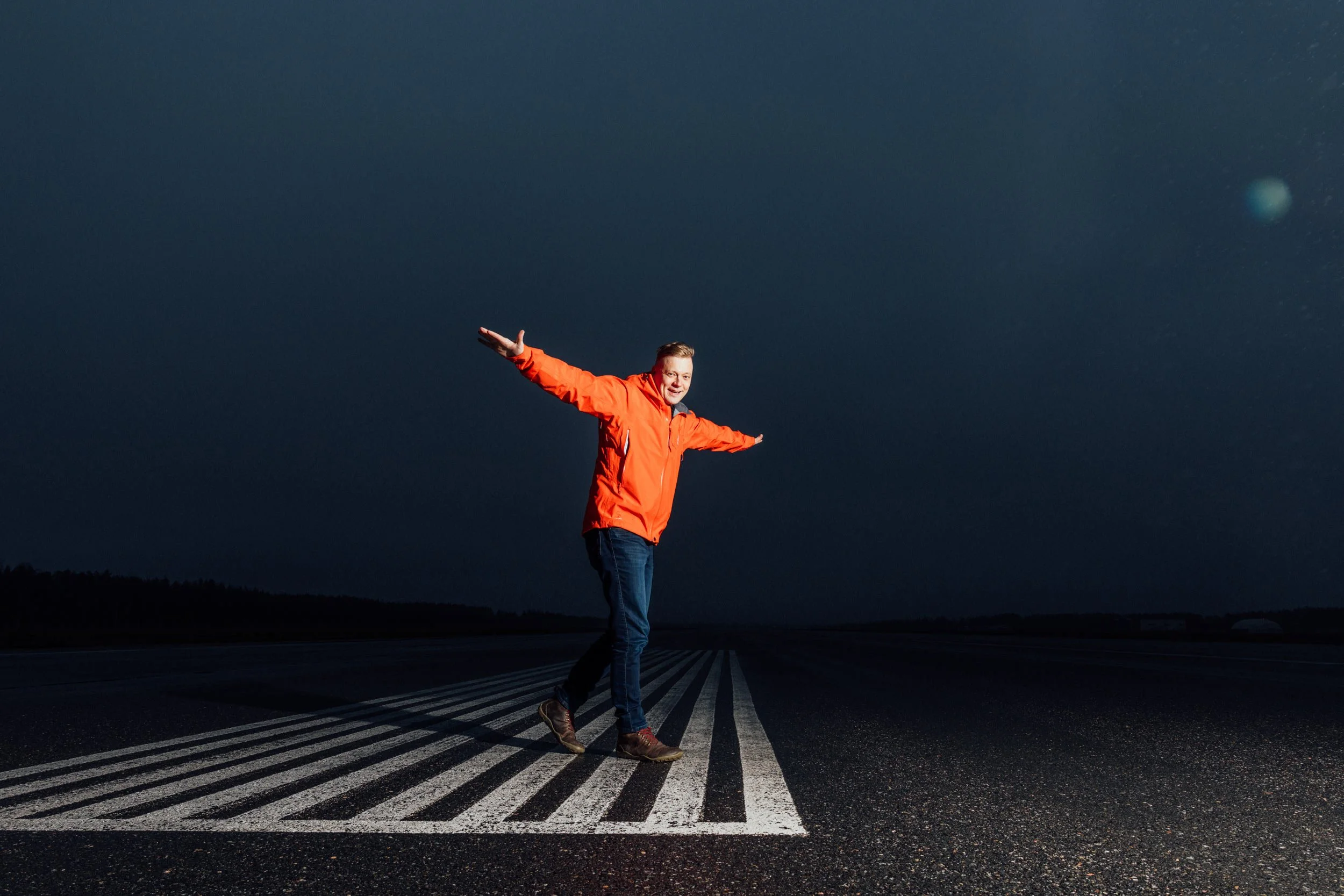 A man standing on a crosswalk at night with arms extended and a night sky background.