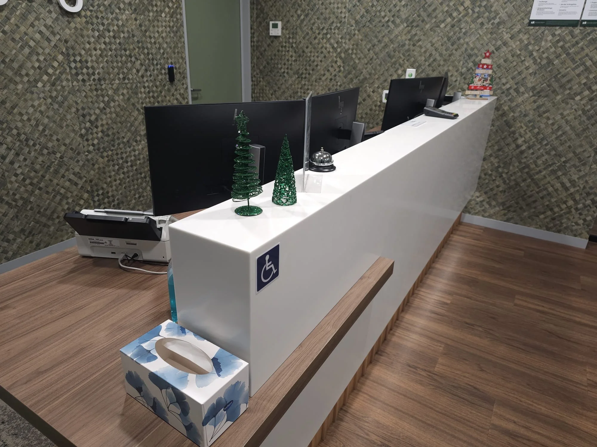 Office reception desk with holiday decorations, including small Christmas trees, a snowman, and a tissue box, with computers, a phone, and a bell visible on the desk.