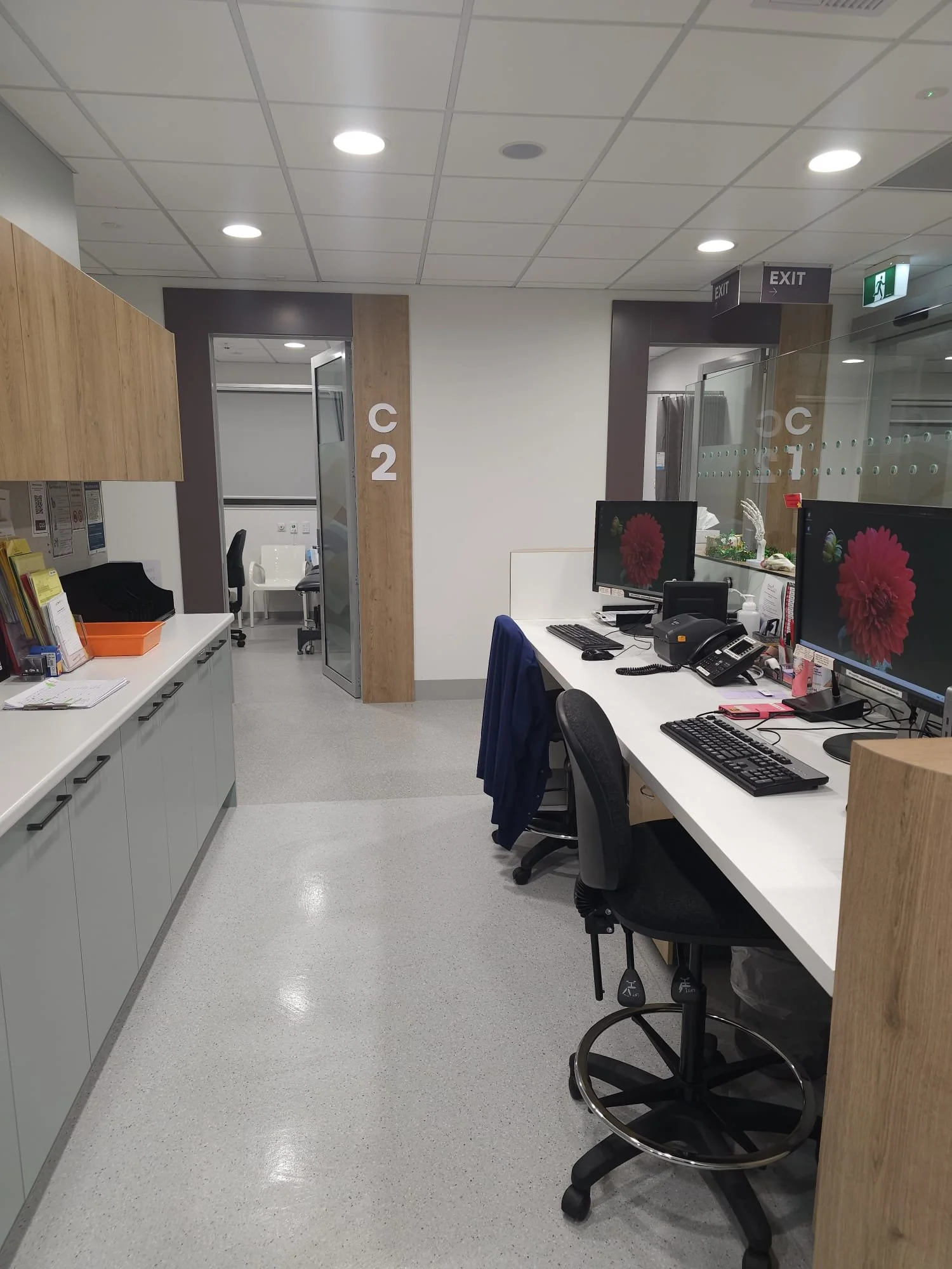 Office reception area with two desk stations featuring computer monitors, keyboards, and telephones, and a door marked 'C2' leading to another room.