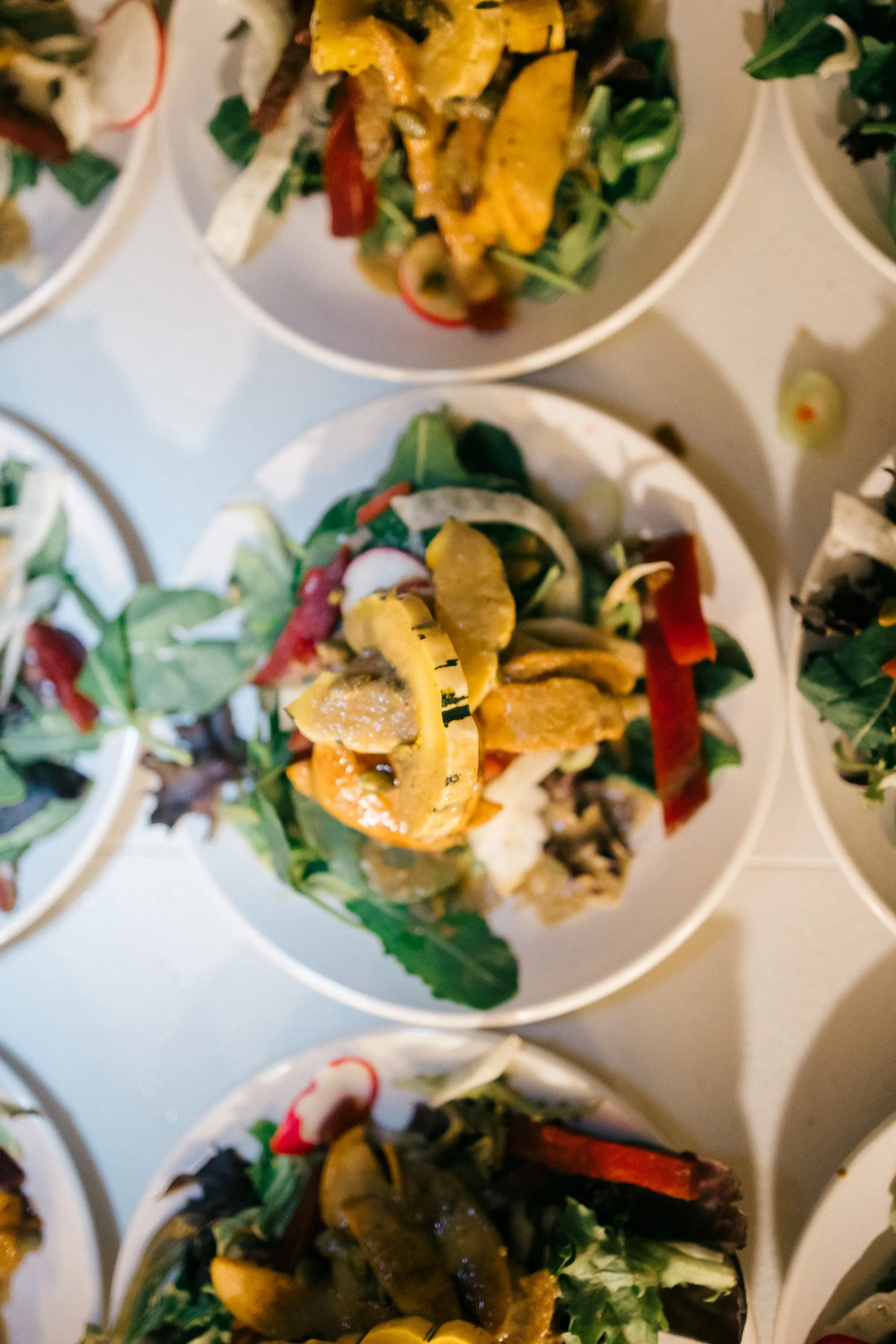Assorted salads in small white bowls, containing vegetables like lettuce, peppers, cucumbers, and toppings such as grilled chicken or other meats, arranged on a white table at Lambert's Cove Inn on Martha's Vineyard.