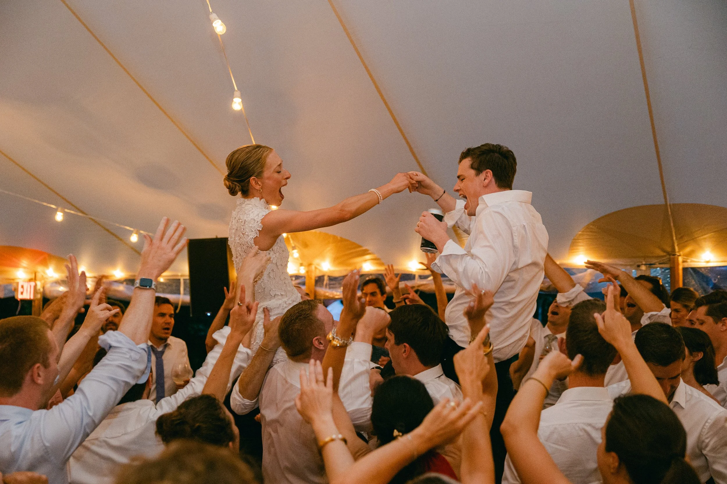 A bride and groom dancing on a crowded dance floor during their wedding reception at Lambert's Cove Inn on Martha's Vineyard under string lights, with guests cheering and reaching up toward them.