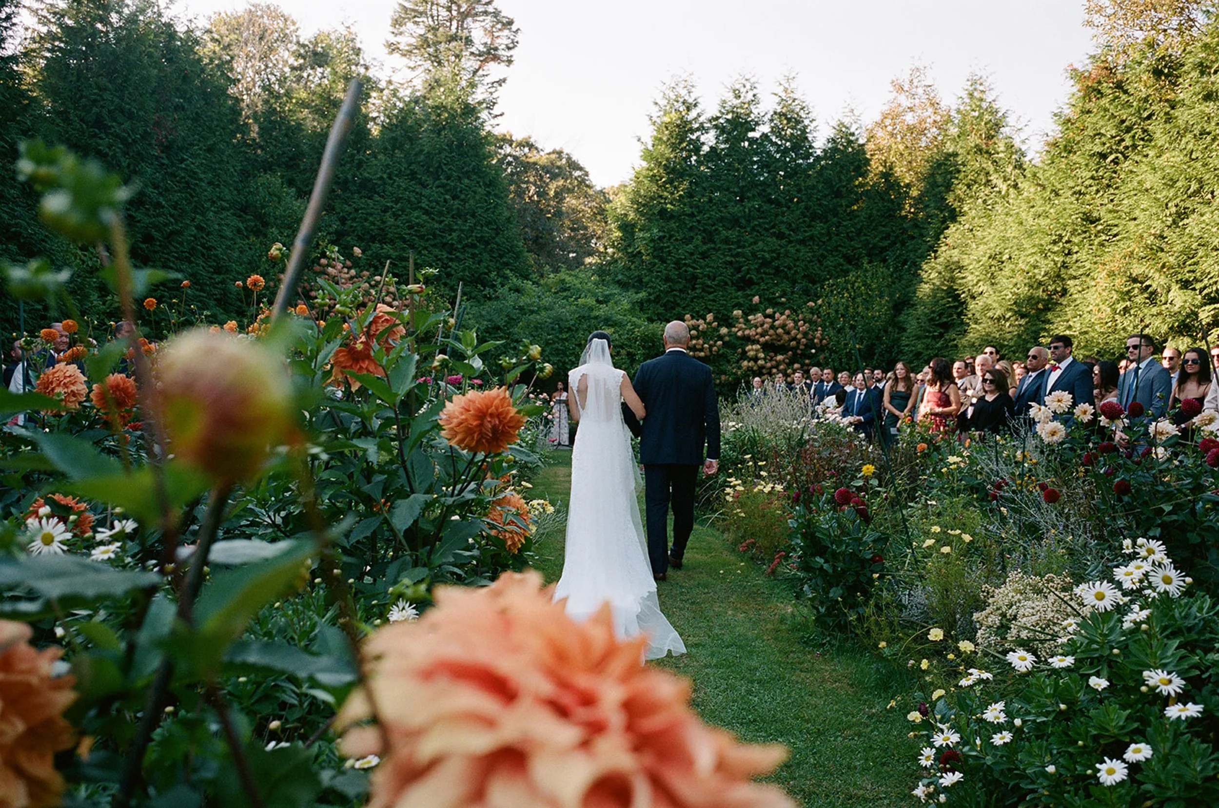 Father of the bride walking the bride in a white wedding gown down the aisle surrounded by beautiful flowers.