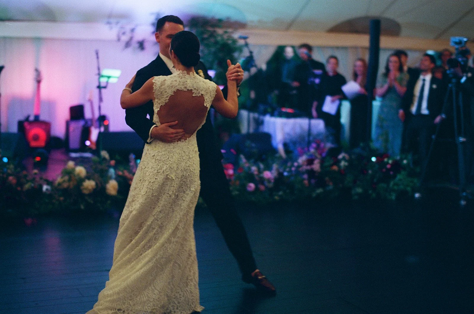 A bride and groom dance at a wedding reception, with blurred guests and floral decorations in the background during a wedding reception at Lambert's Cove Inn on Martha's Vineyard.
