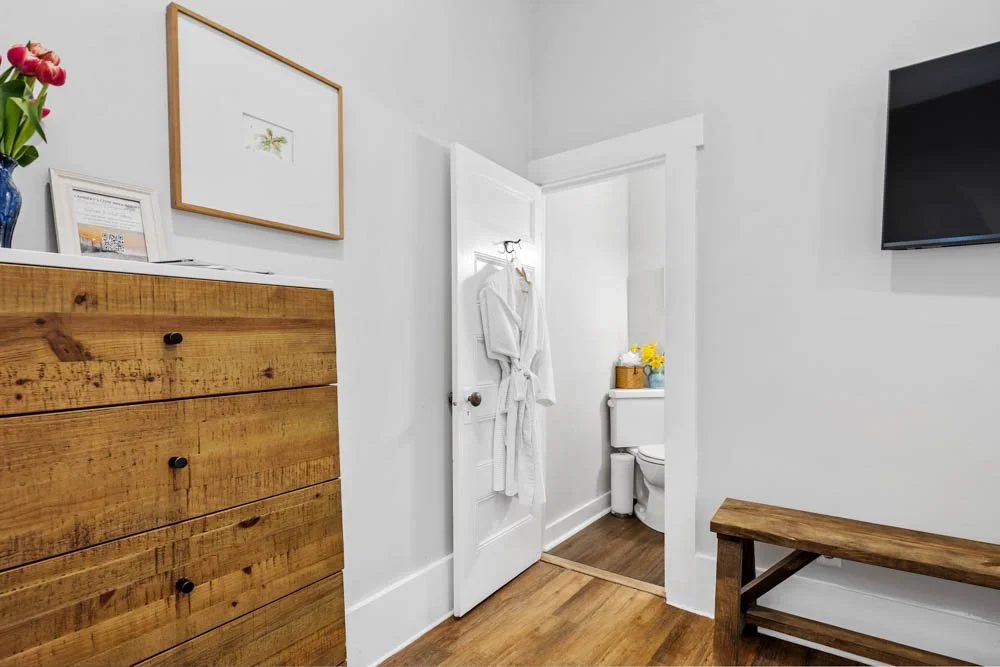Interior view of a bedroom with an open door leading to a bathroom, wooden furniture, and decor.